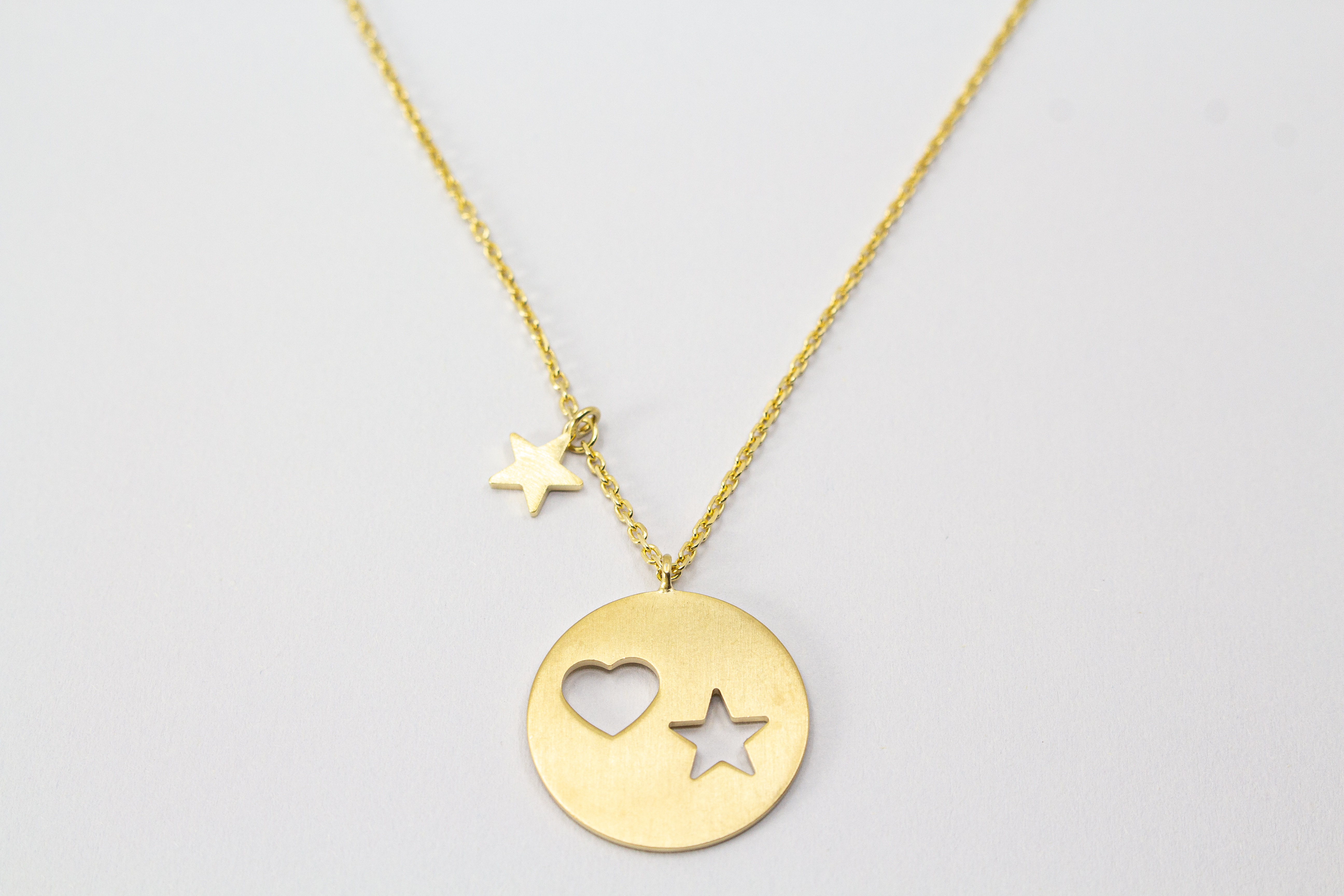 Collier „Sternenliebe“ aus vergoldetem 925er Sterlingsilber mit rundem Anhänger, Herz- und Sternmotiv sowie zusätzlichem Sternanhänger.
