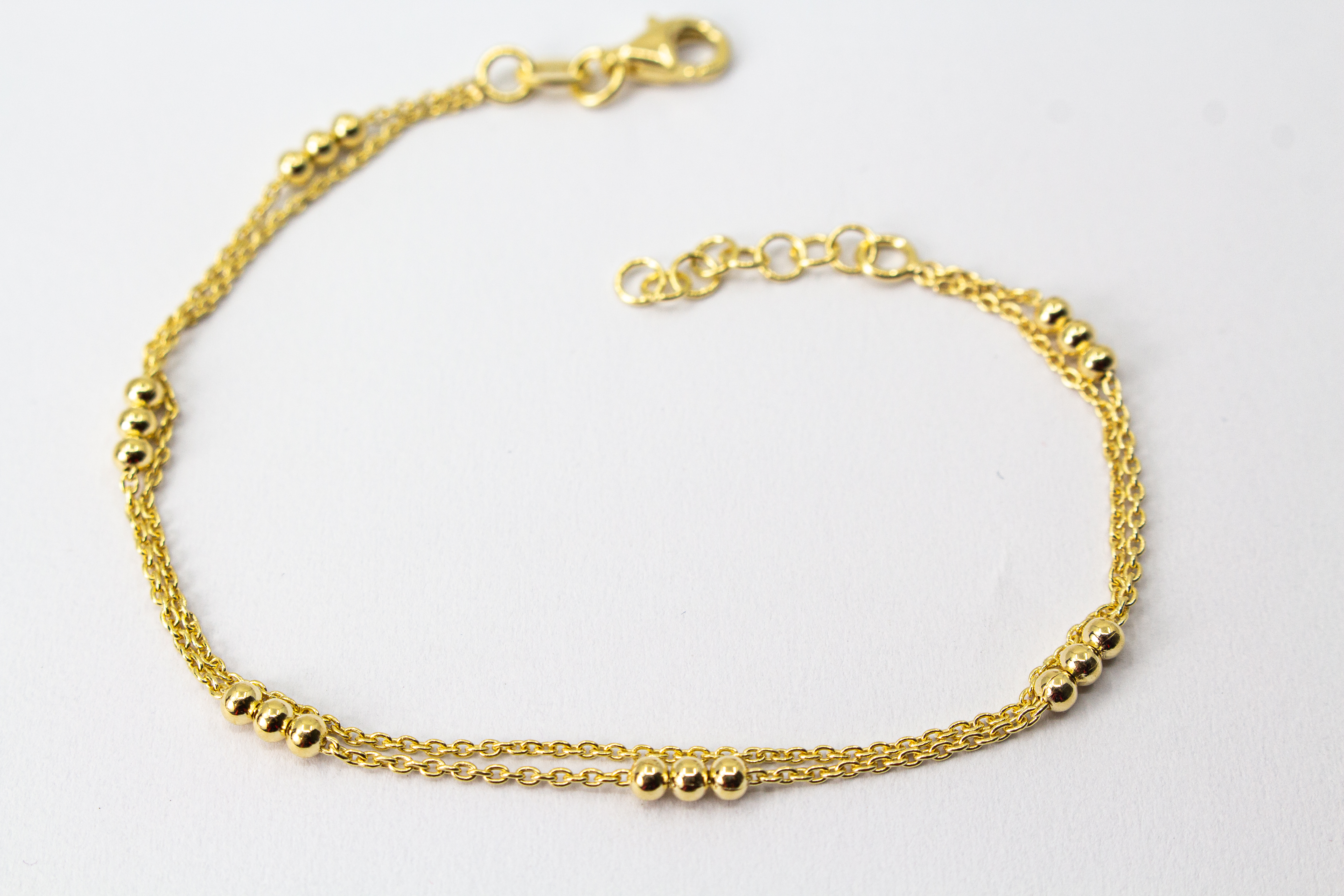 Zartes, zweireihiges Armband aus vergoldetem 925er Silber mit kleinen Goldkugeln, die in Dreiergruppen auf zwei feinen Ankerketten angeordnet sind.
