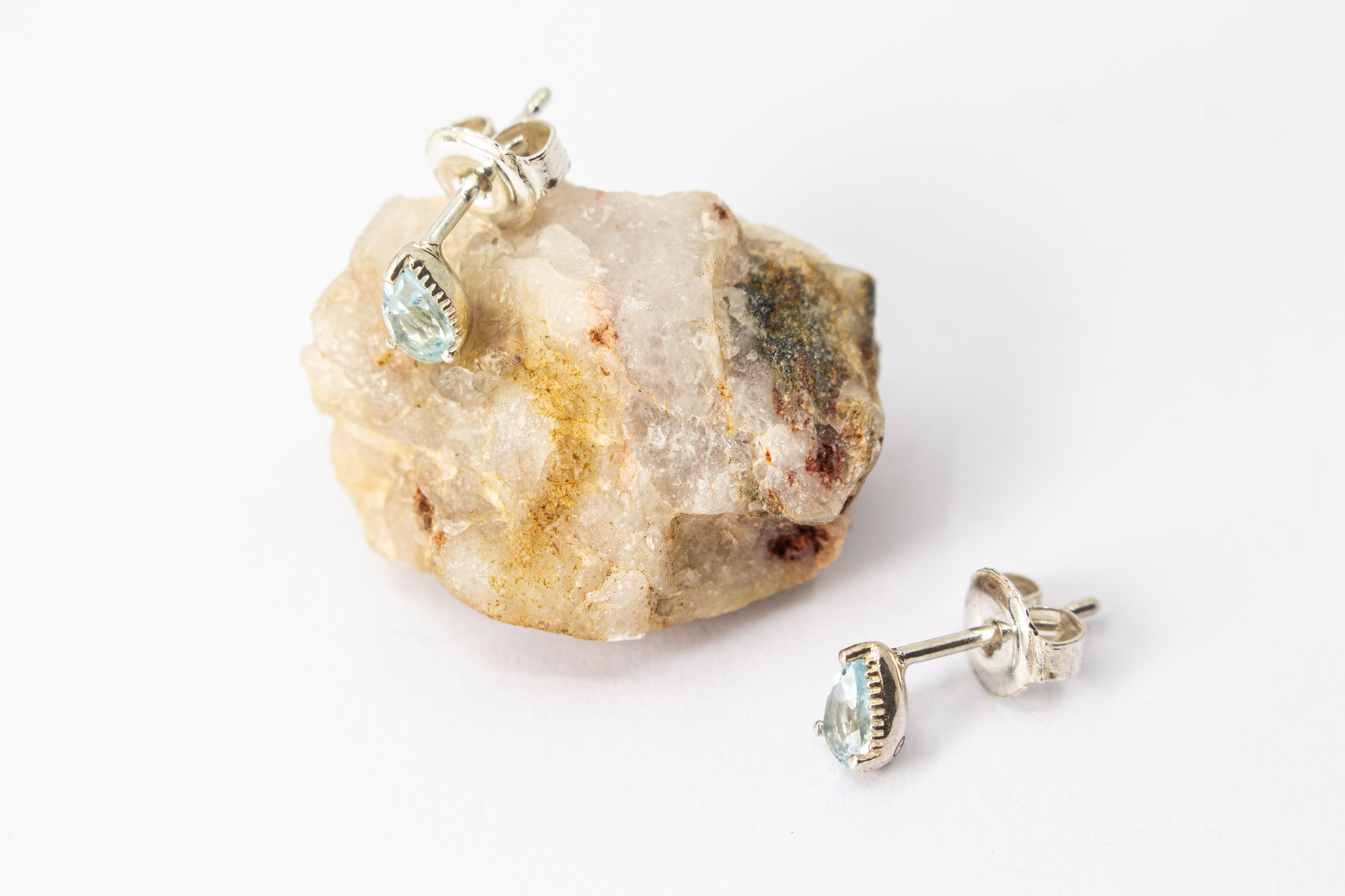 filigrane Ohrstecker aus glänzendem 925 Sterling Silber mit kleinen, tropfenförmigen, hellblauen Topas-Edelsteinen in einer fein verzierten Krappenfassung aus dem Online-Shop der Goldschmiede Regina Kraus.