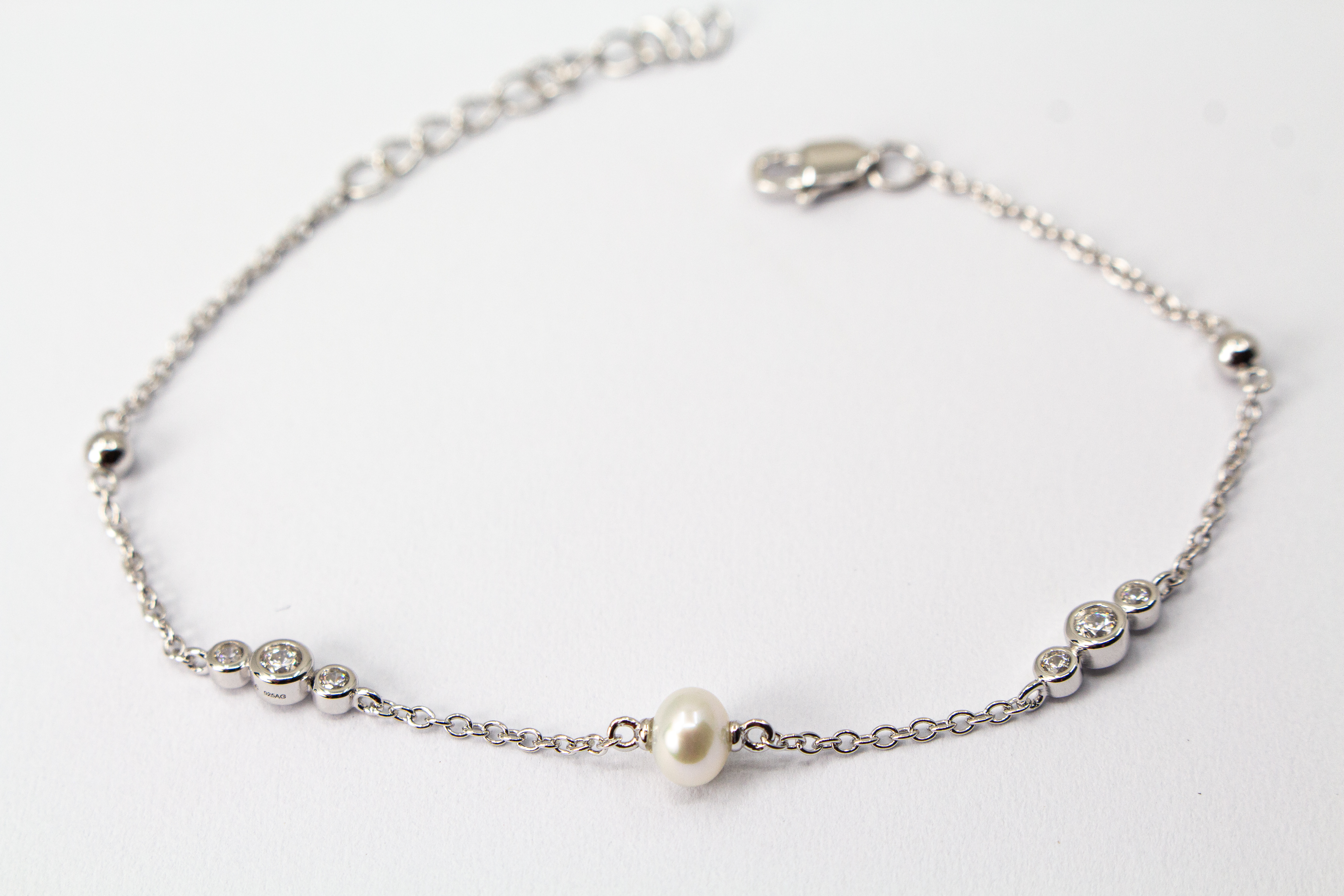 Zartes Armkettchen 'Pearl and Glint' aus rhodiniertem 925er Sterlingsilber mit einer zentralen Süßwasserzuchtperle und seitlichen Zirkonia-Einsätzen,