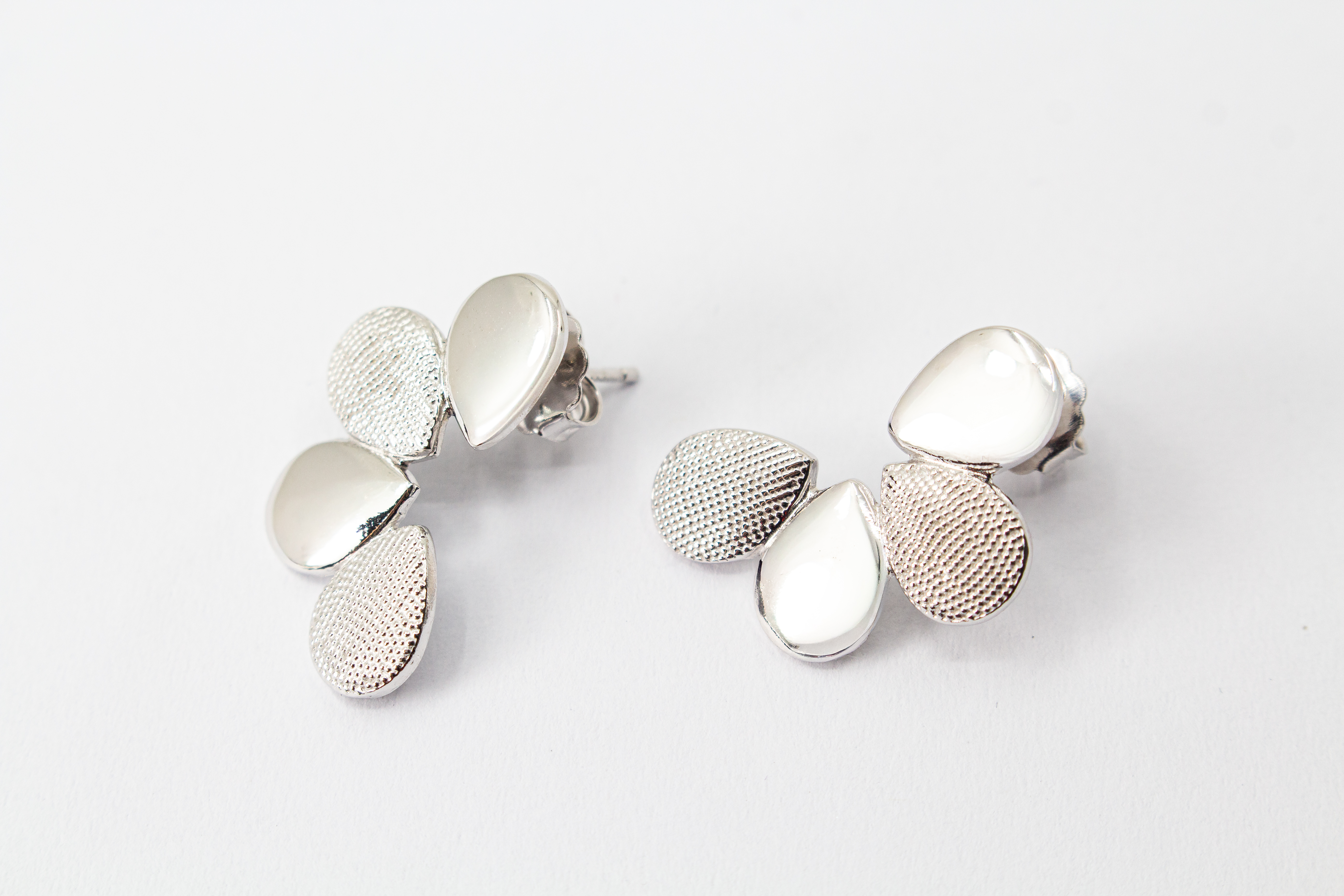 Moderne Ohrstecker der Cosmic Drop Serie von Diva Gioielli aus rhodiniertem 925 Silber. Die Ohrringe zeigen eine fächerförmige Anordnung von glatten und punktförmig strukturierten Tropfen