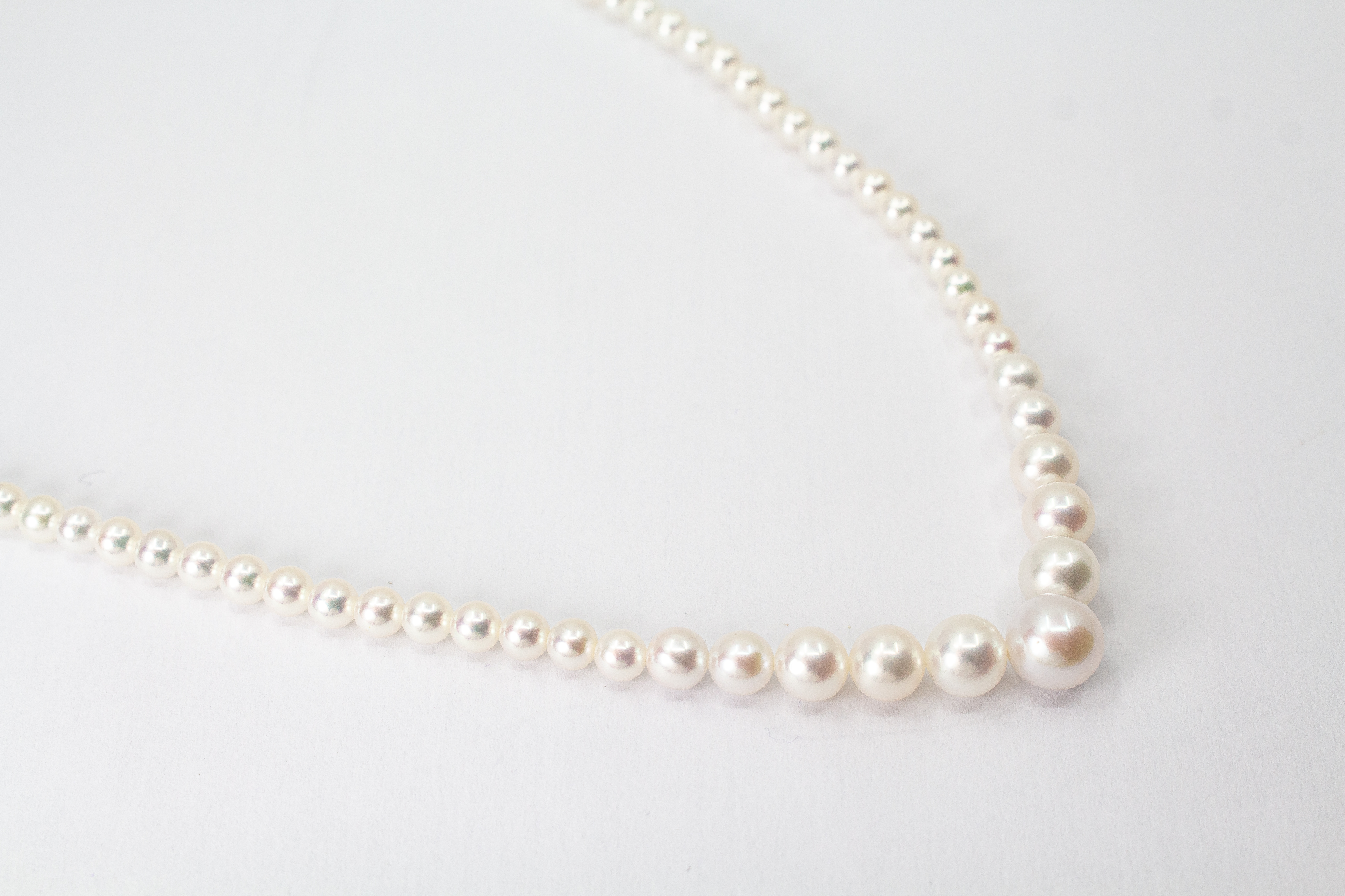 Eine klassische Süßwasserzuchtperlenkette von der Goldschmiede Regina Kraus, elegant geschwungen auf weißem Hintergrund ausgelegt. Die runden Perlen weisen einen zarten, cremeweißen Lüster auf und sind im harmonischen Verlauf angeordnet, wobei die größte