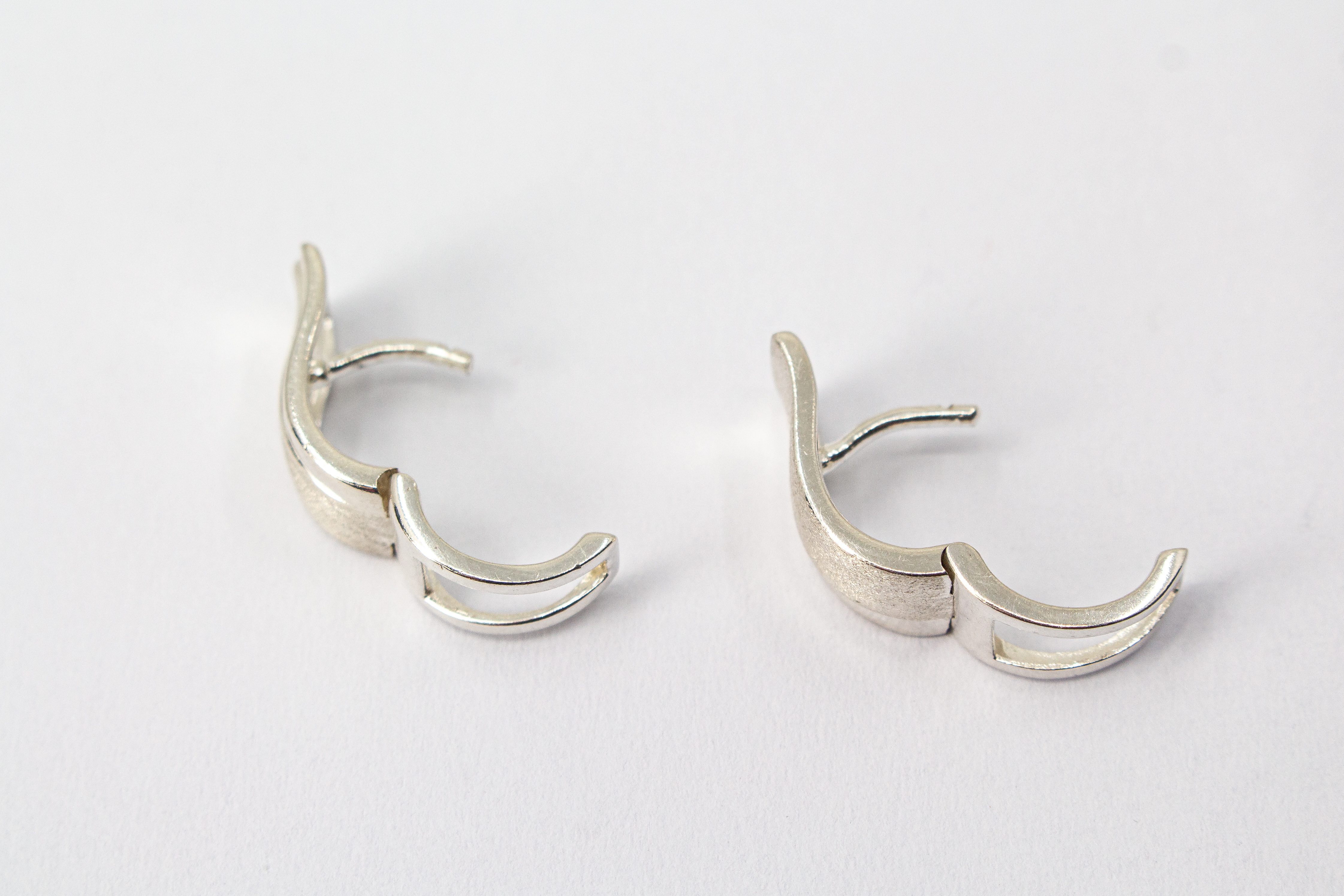 Breite Klappcreolen aus 925er Silber mit einer schwungvoll hochgezogenen, eismattierten Vorderseite und glänzend polierten Kanten im Onlineshop von Goldschmiede Regina Kraus.