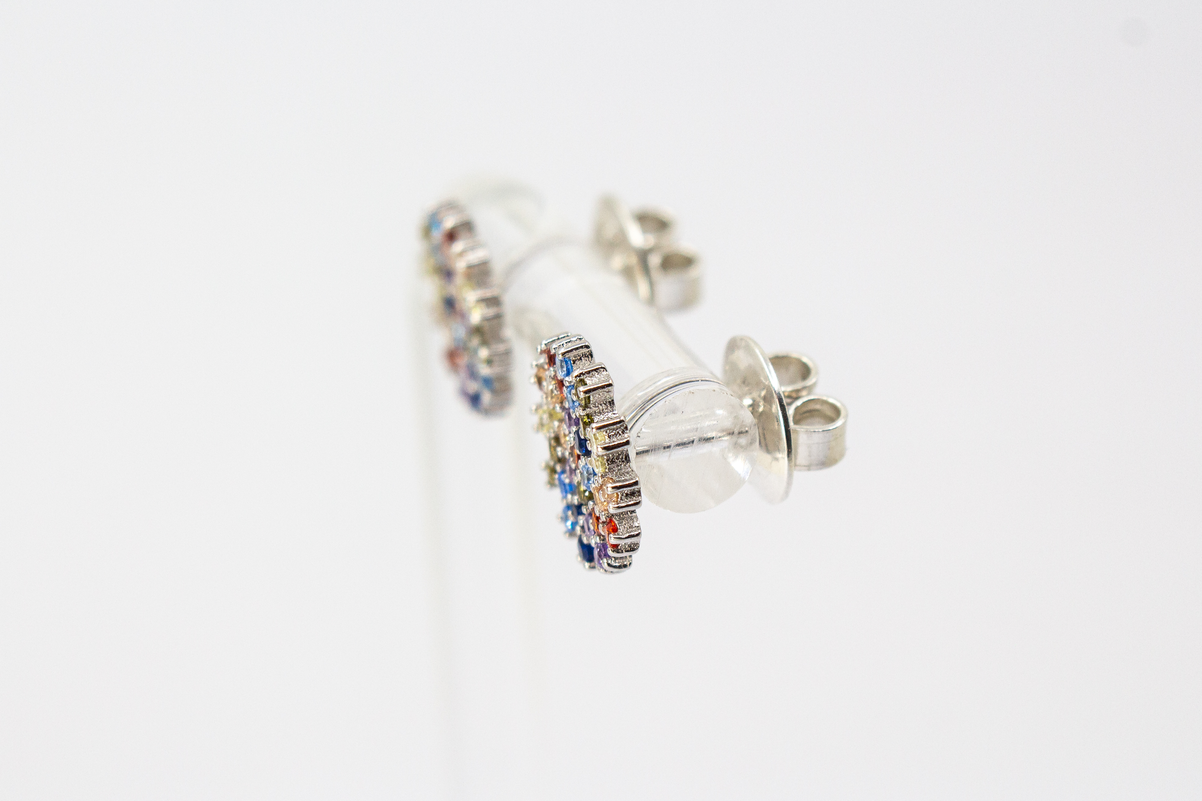 Die filigranen 925er Silber-Ohrstecker „Fleur de Lumière“ aus der Goldschmiede Regina Kraus, präsentiert auf einem transparenten Schmuckständer. Das florale Design erinnert an eine funkelnde Lichtblume und ist kunstvoll mit kleinen, bunt strahlenden Zirk