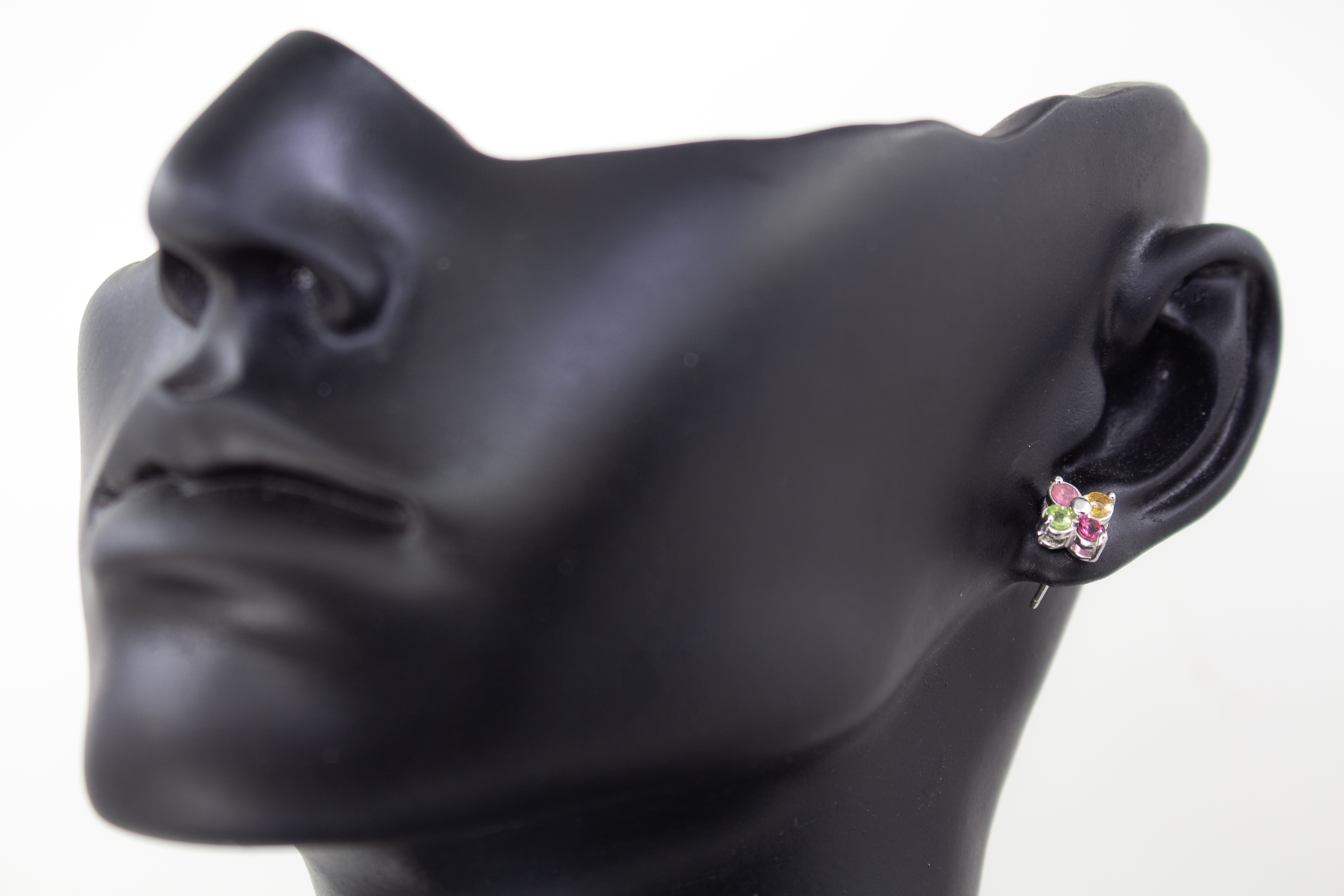 Die filigranen Silber-Ohrstecker „Elfenblüte“ aus der Goldschmiede Regina Kraus an einem transparenten Halter. Die Stecker aus rhodiniertem 925er Sterlingsilber zeigen eine zarte Blütenform, besetzt mit vier bunten Turmalinen in Rosé, Grün und Gelb um ei