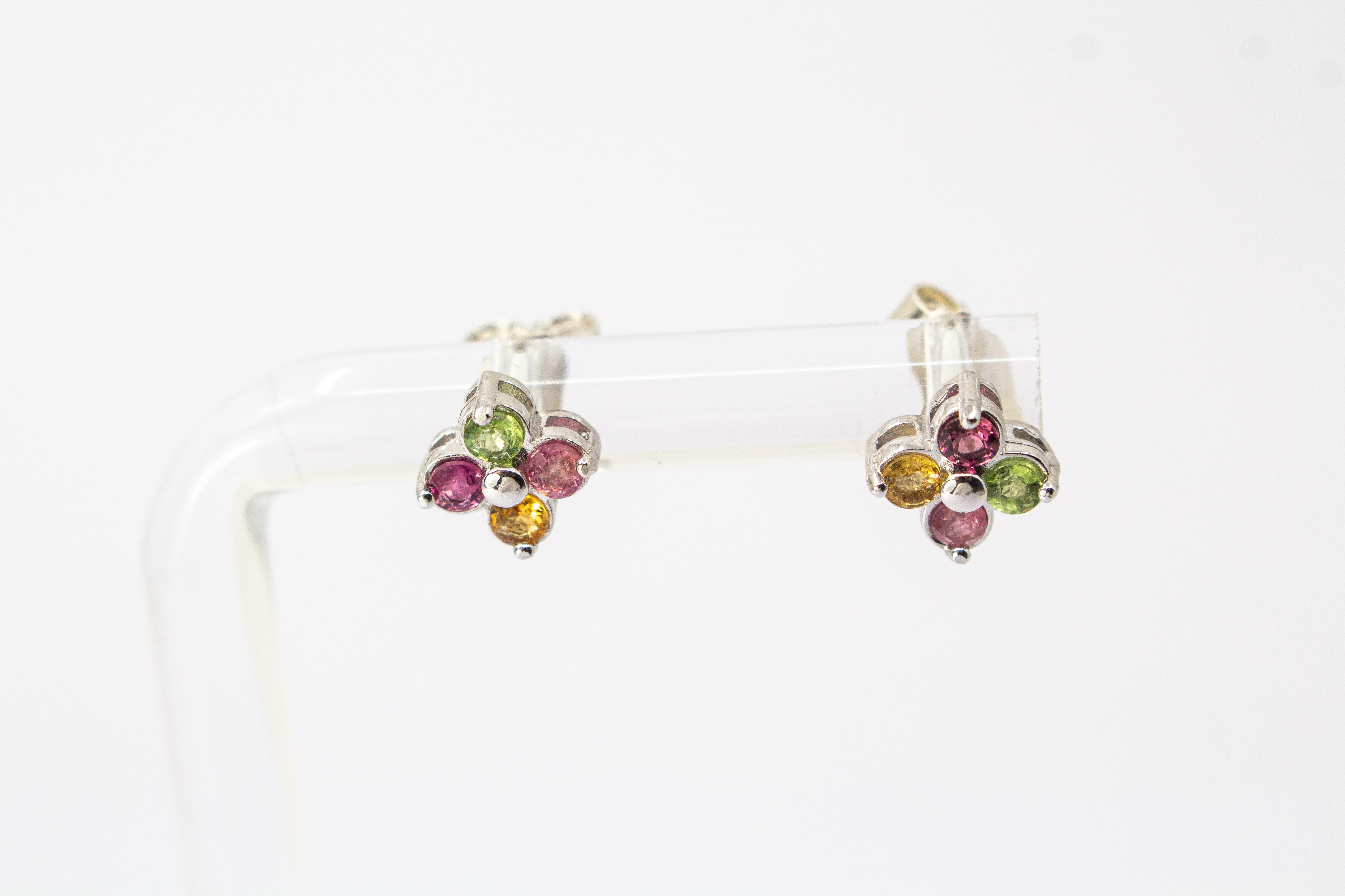 Die filigranen Silber-Ohrstecker „Elfenblüte“ aus der Goldschmiede Regina Kraus an einem transparenten Halter. Die Stecker aus rhodiniertem 925er Sterlingsilber zeigen eine zarte Blütenform, besetzt mit vier bunten Turmalinen in Rosé, Grün und Gelb um ei