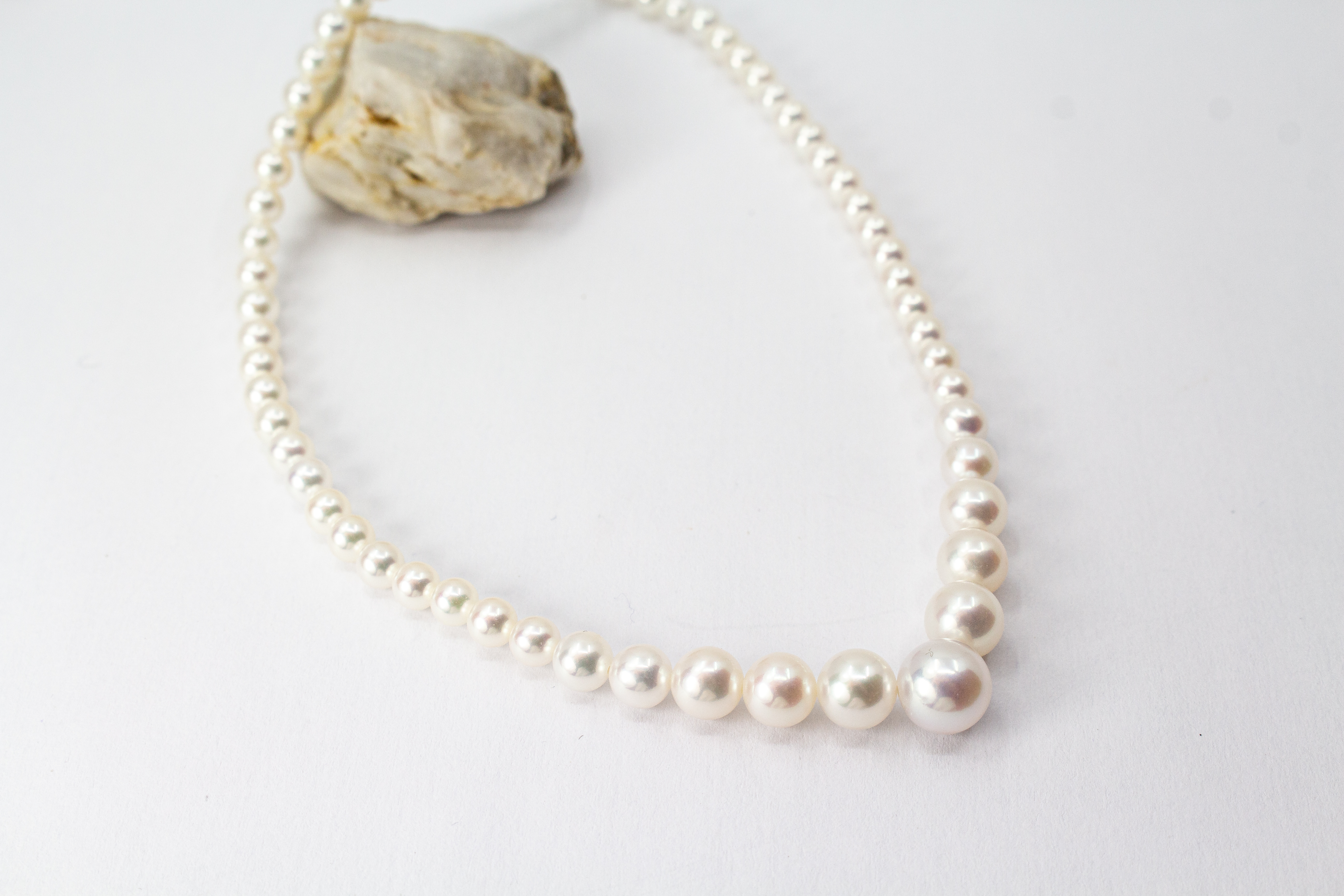 Eine klassische Süßwasserzuchtperlenkette von der Goldschmiede Regina Kraus, elegant geschwungen auf weißem Hintergrund ausgelegt. Die runden Perlen weisen einen zarten, cremeweißen Lüster auf und sind im harmonischen Verlauf angeordnet, wobei die größte