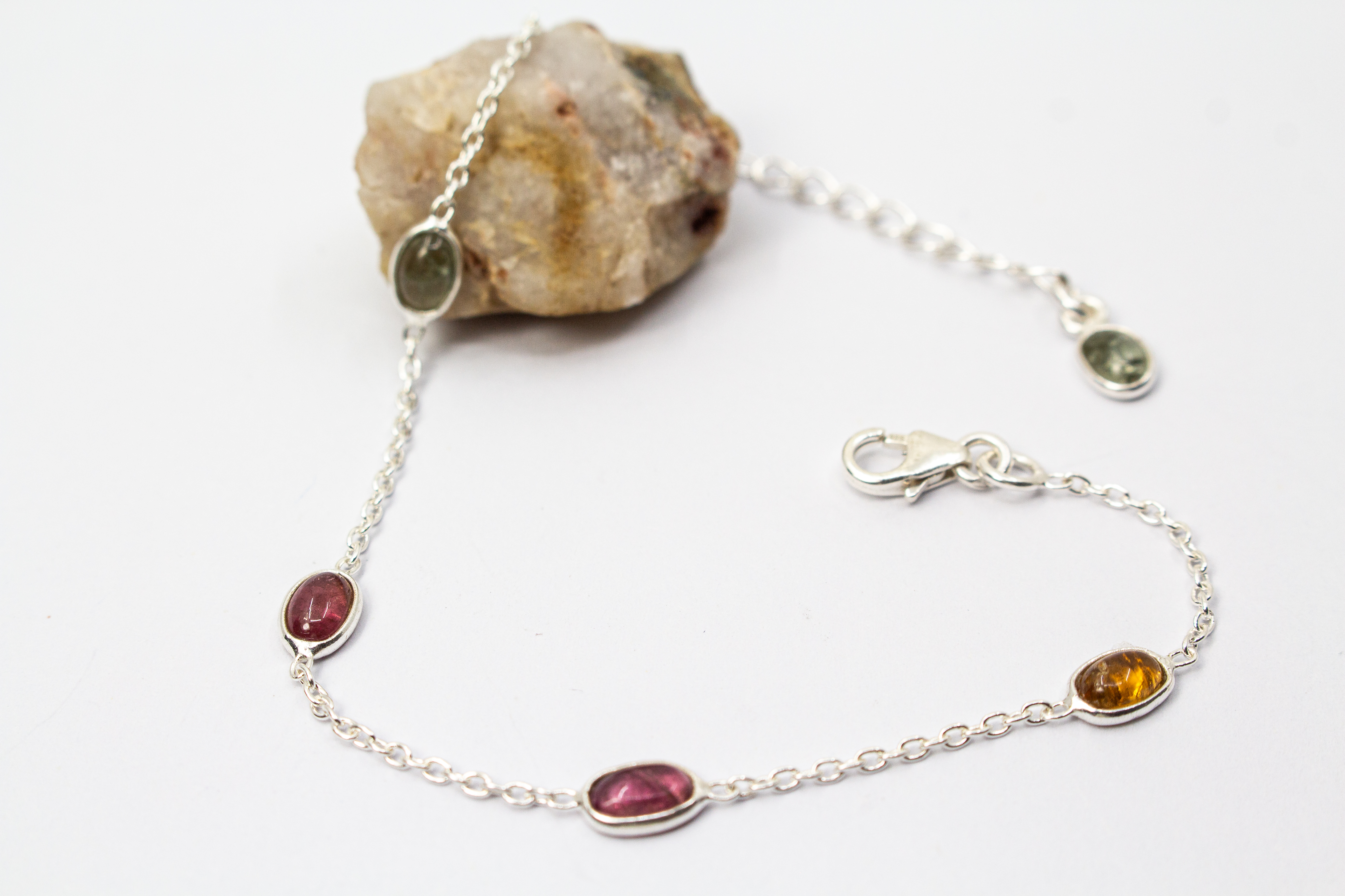 Das filigrane Silber-Armband „Indian Summer“ aus der Goldschmiede Regina Kraus, flach auf weißem Untergrund arrangiert. Die feine Kette aus rhodiniertem 925er Sterlingsilber verbindet fünf ovale Turmalin-Cabochons in den warmen Farben Weinrot, Moosgrün, R