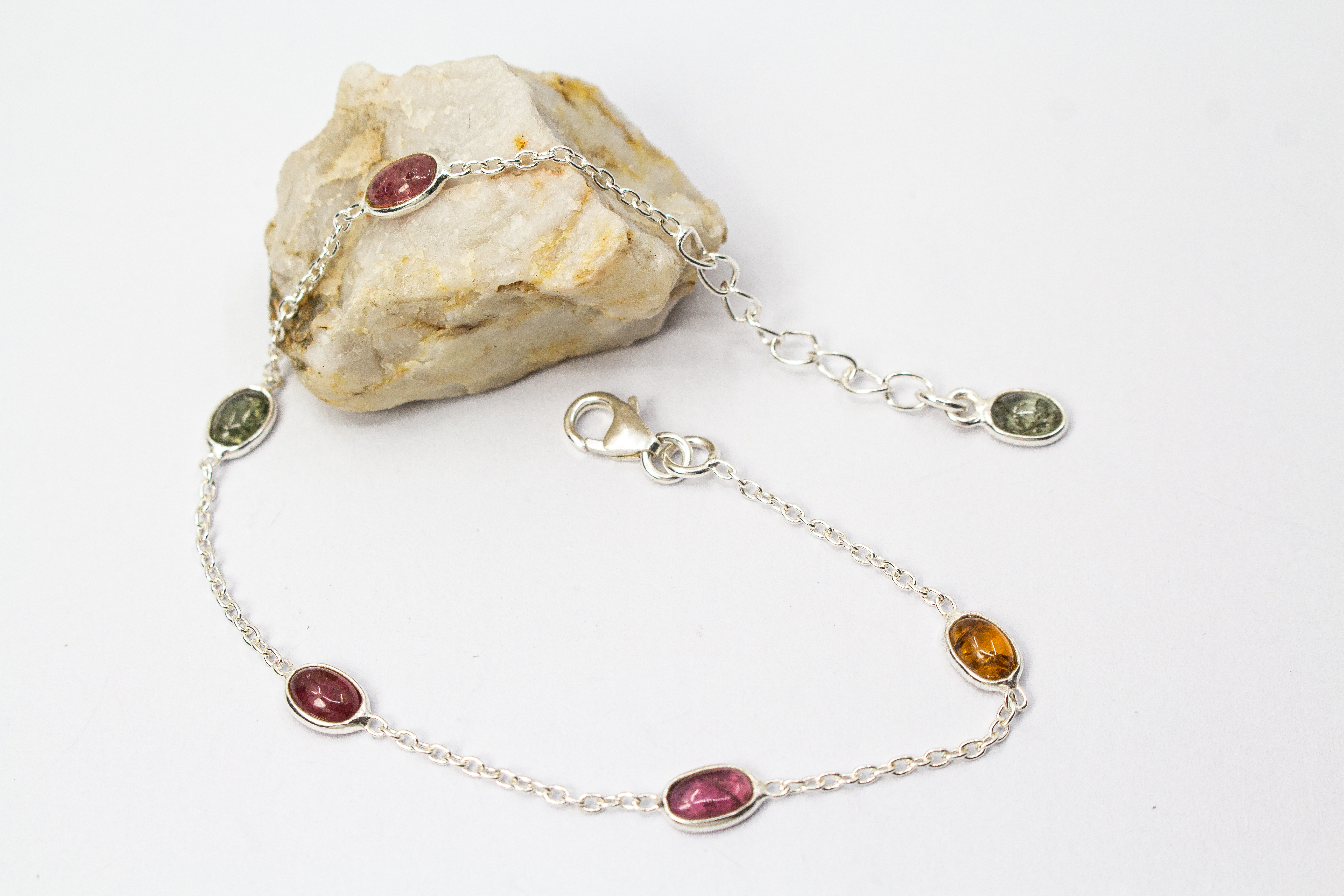Das filigrane Silber-Armband „Indian Summer“ aus der Goldschmiede Regina Kraus, flach auf weißem Untergrund arrangiert. Die feine Kette aus rhodiniertem 925er Sterlingsilber verbindet fünf ovale Turmalin-Cabochons in den warmen Farben Weinrot, Moosgrün, R