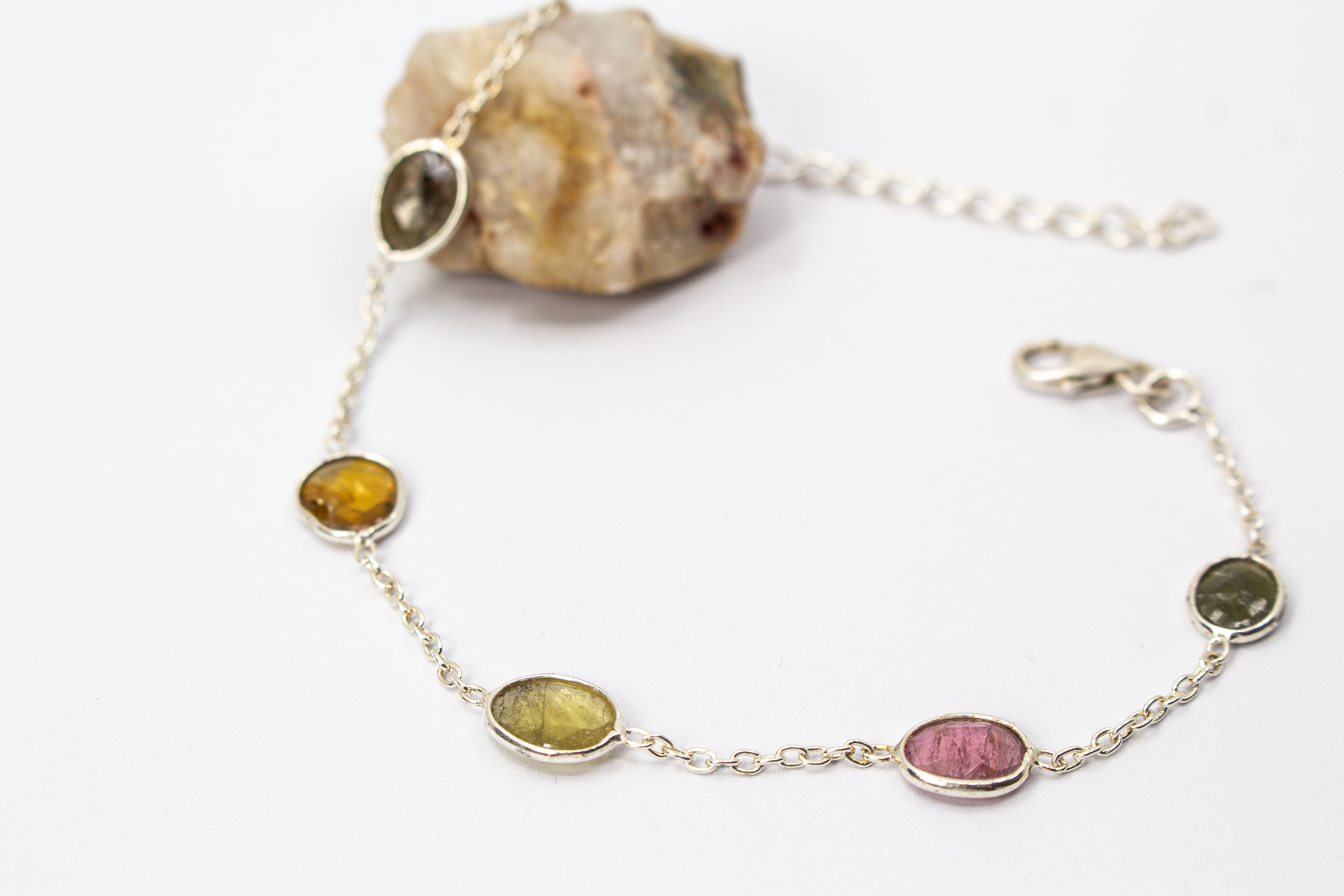 Ein filigranes Armband aus 925 Sterlingsilber von der Goldschmiede Regina Kraus, flach auf weißem Hintergrund arrangiert. In die feine Gliederkette sind sechs verschiedenfarbige, flache Turmaline in ovalen Zargenfassungen eingearbeitet – darunter Gelb-,