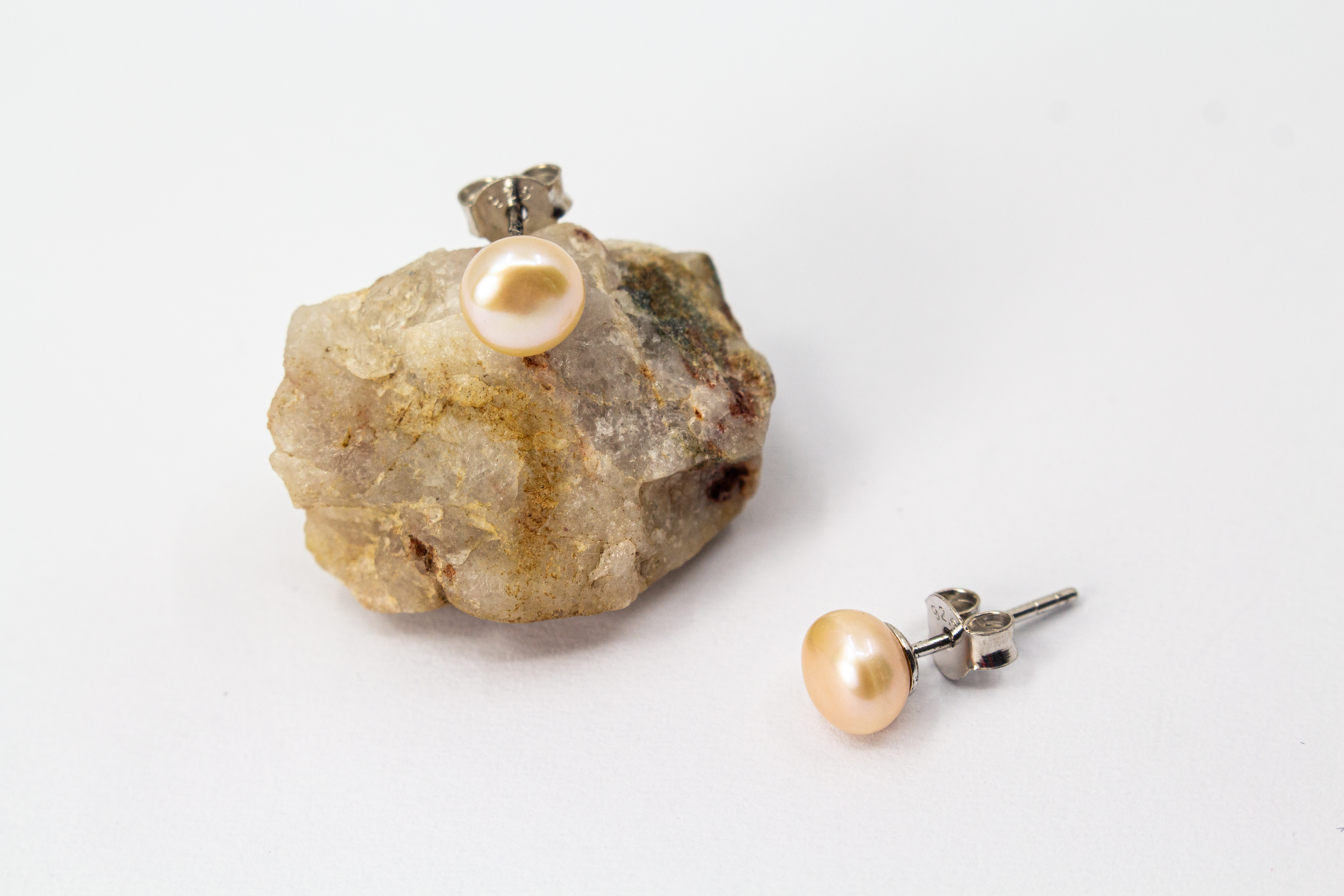 Ein Paar klassische Damen-Ohrstecker aus poliertem 925 Sterlingsilber mit je einer runden, lachsfarbenen Süßwasserzuchtperle, präsentiert von der Goldschmiede Regina Kraus.