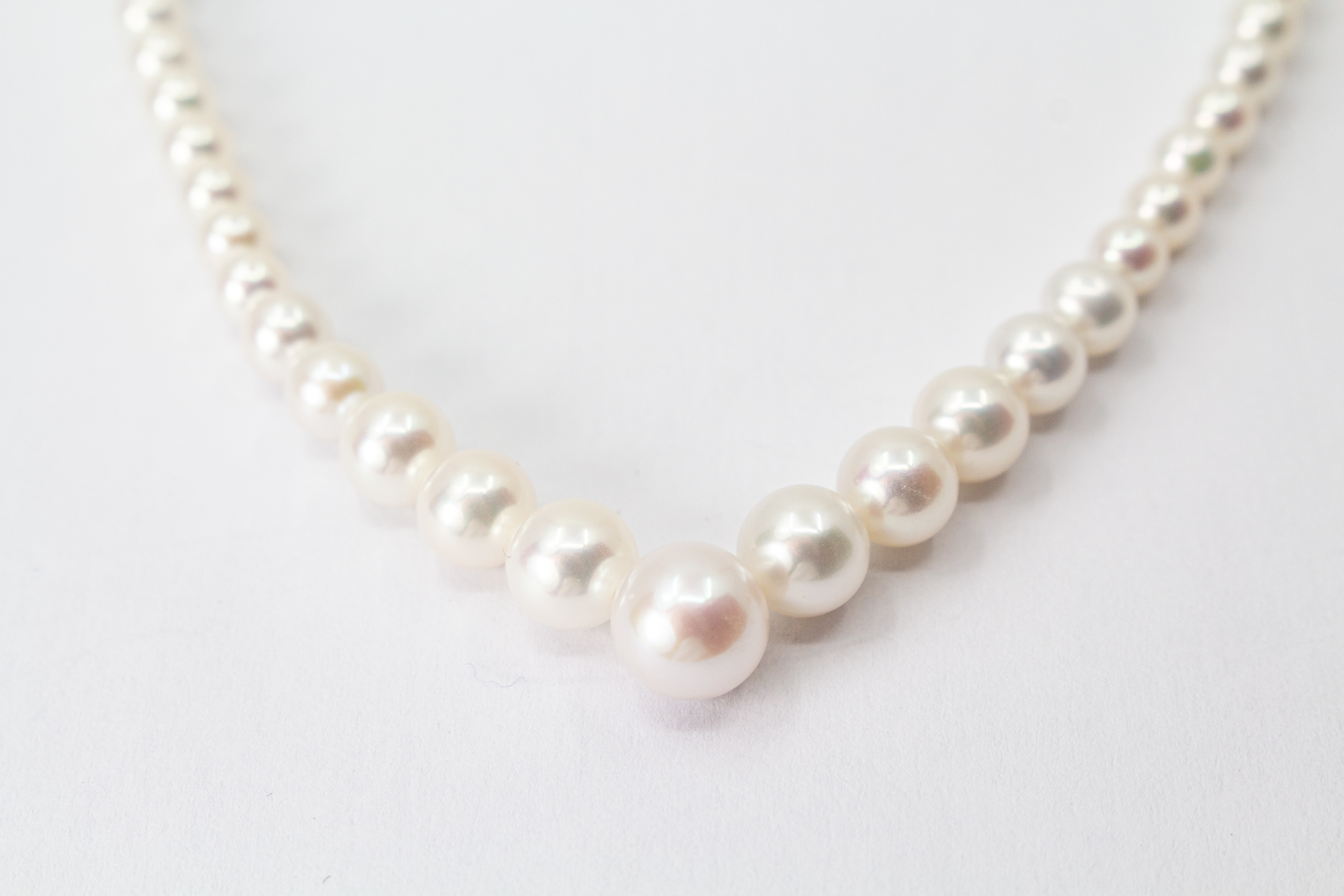 Eine klassische Süßwasserzuchtperlenkette von der Goldschmiede Regina Kraus, elegant geschwungen auf weißem Hintergrund ausgelegt. Die runden Perlen weisen einen zarten, cremeweißen Lüster auf und sind im harmonischen Verlauf angeordnet, wobei die größte