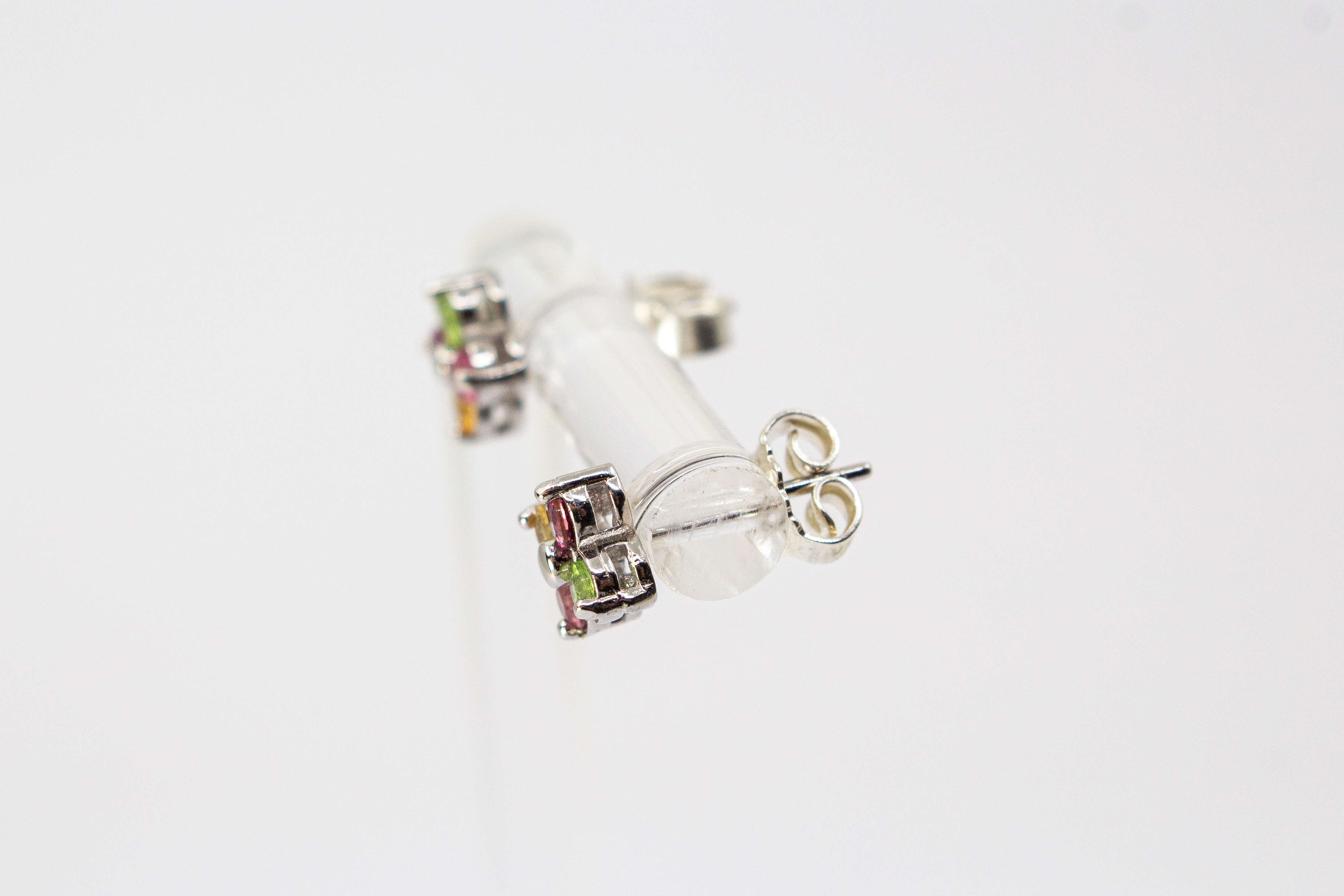 Die filigranen Silber-Ohrstecker „Elfenblüte“ aus der Goldschmiede Regina Kraus an einem transparenten Halter. Die Stecker aus rhodiniertem 925er Sterlingsilber zeigen eine zarte Blütenform, besetzt mit vier bunten Turmalinen in Rosé, Grün und Gelb um ei