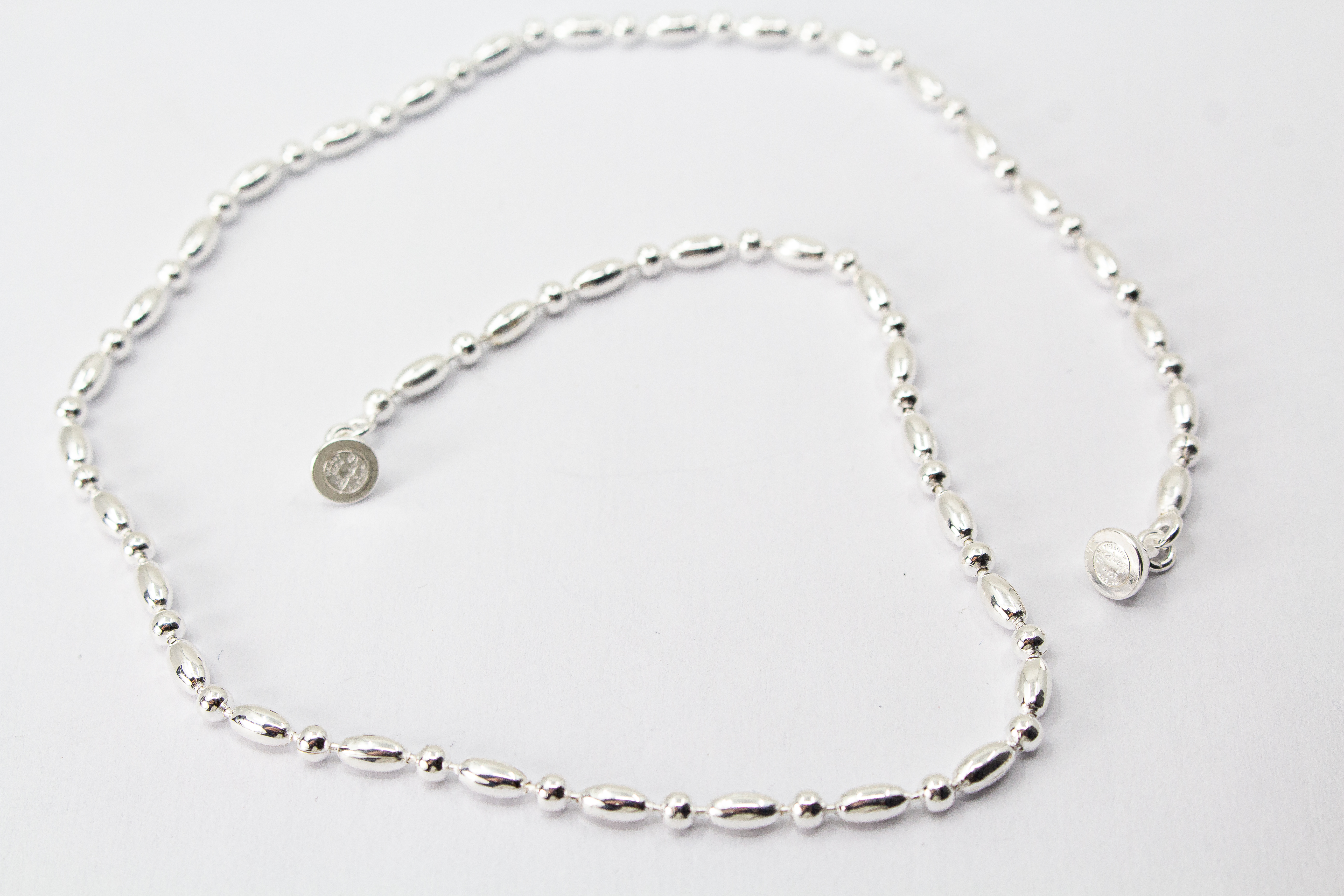Filigrane Silberkette aus hochglanzpoliertem 925er Sterlingsilber mit einem rhythmischen Wechsel aus Oliven- und Kugel-Elementen auf hellem Untergrund, exklusiv erhältlich im Schmuck-Onlineshop der Goldschmiede Regina Kraus.