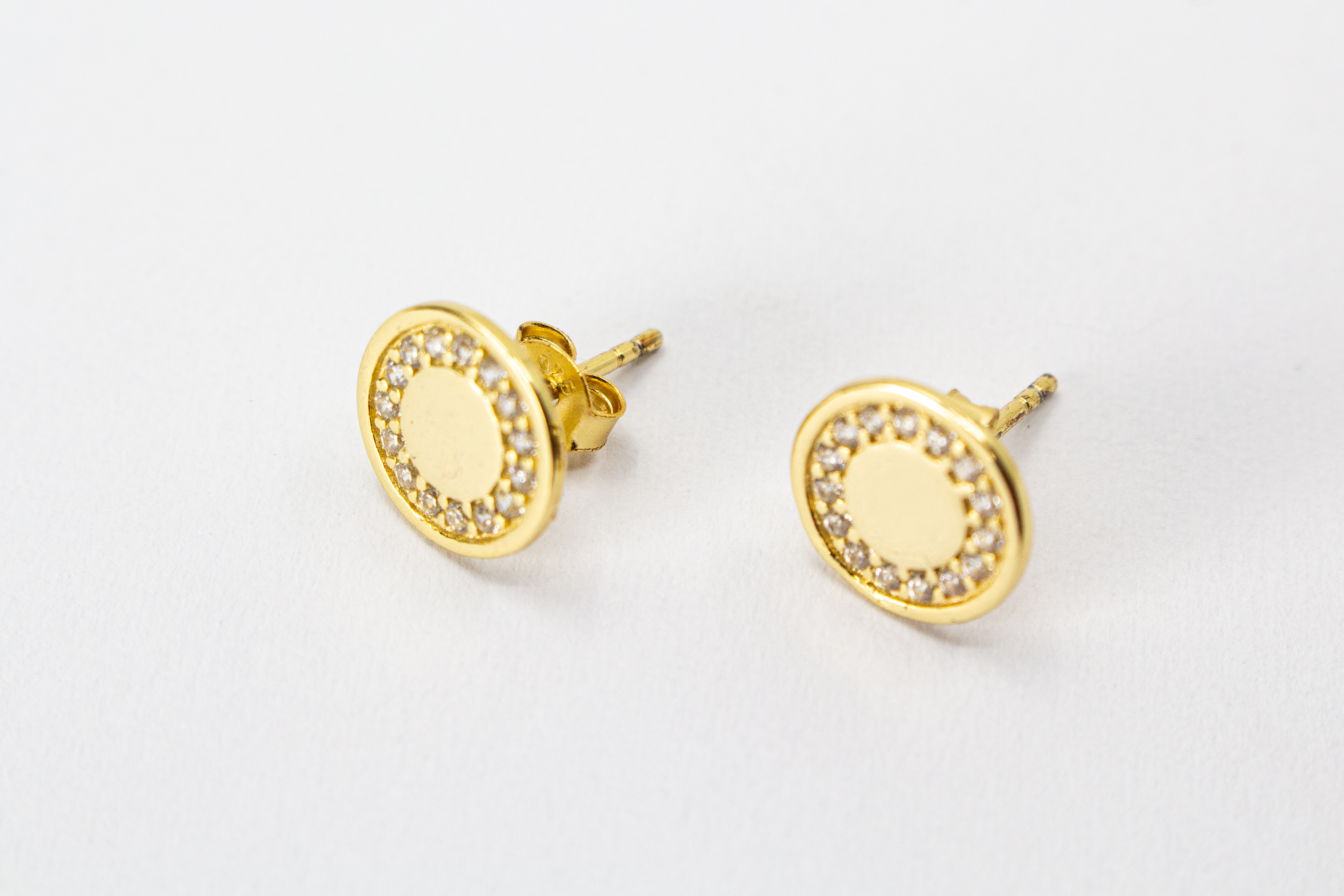 Runde, vergoldete Ohrstecker aus 925er Silber mit einer glatten Innenfläche und einem äußeren Kranz aus funkelnden Zirkoniasteinen im Onlineshop von Goldschmiede Regina Kraus.