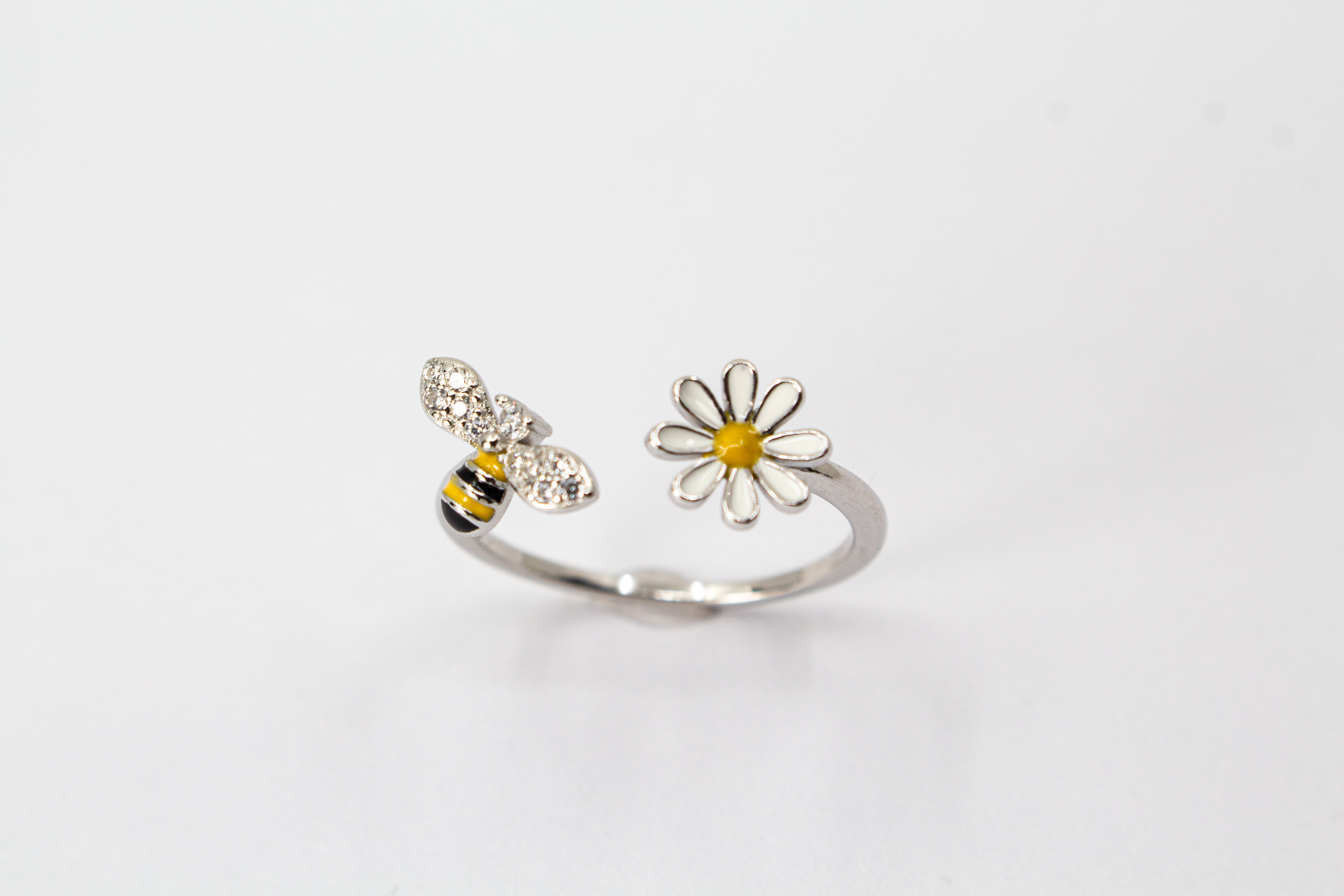 Offener Ring „Blütenbesuch“ aus rhodiniertem 925er Sterlingsilber mit Emaille-Blüte, funkelnder Biene und weißen Zirkonia.
