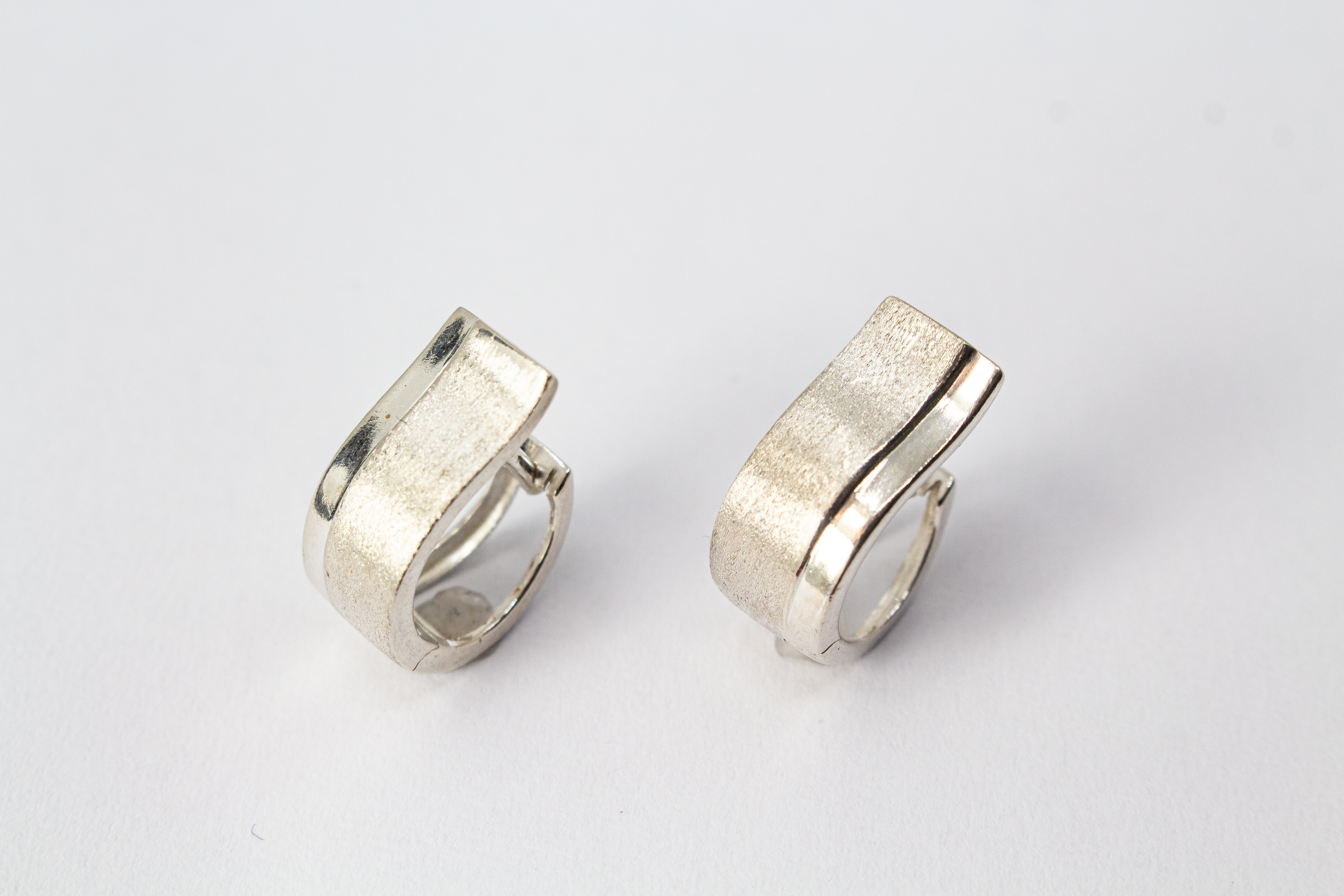Breite Klappcreolen aus 925er Silber mit einer schwungvoll hochgezogenen, eismattierten Vorderseite und glänzend polierten Kanten im Onlineshop von Goldschmiede Regina Kraus.