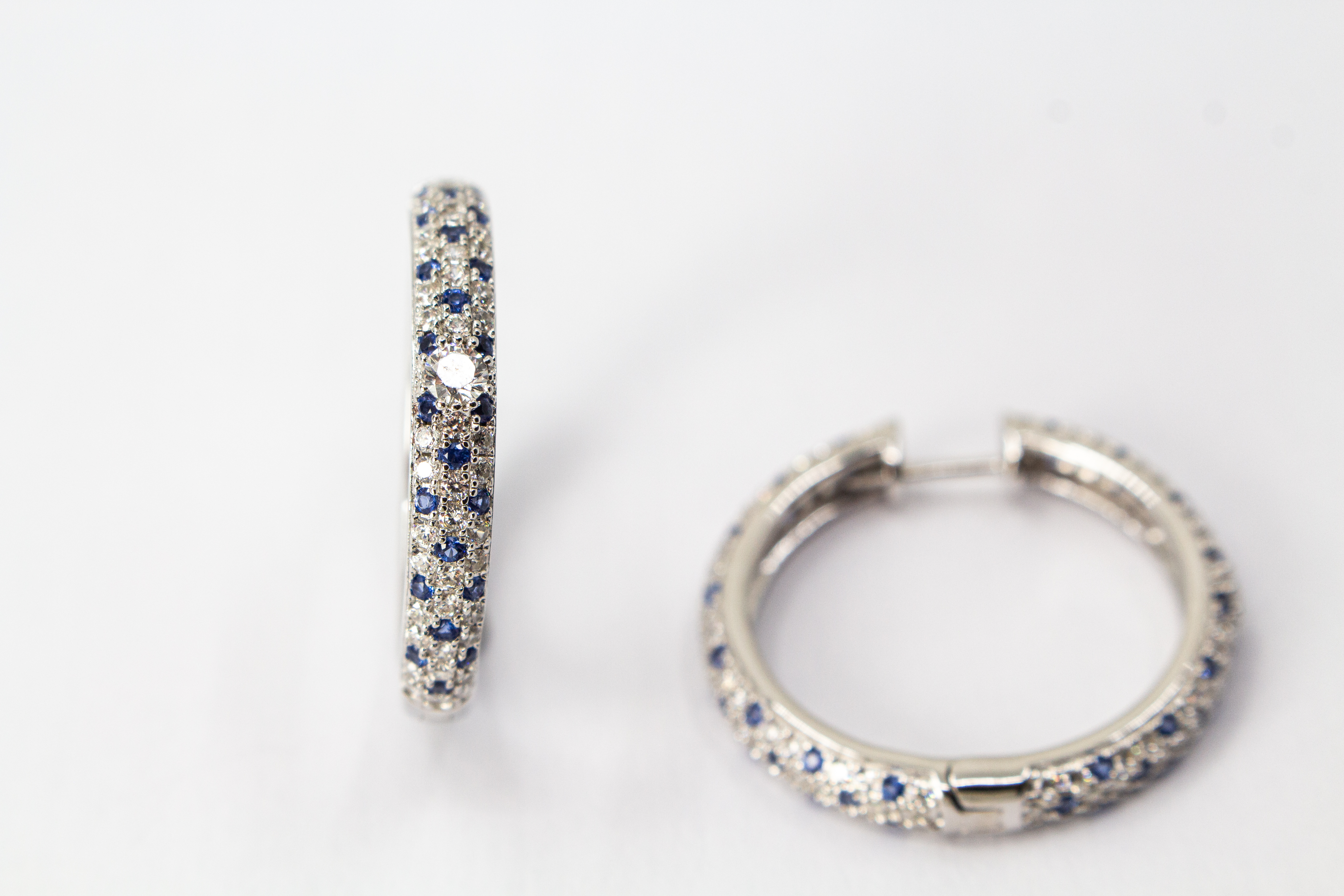 Ein Paar luxuriöse, rhodinierte Klappcreolen aus 925er Sterlingsilber von der Goldschmiede Regina Kraus. Die breite Außenseite ist dreireihig im edlen Pavé-Stil mit funkelnden, weißen und saphirblauen Zirkonia-Steinen besetzt. Eine Creole lehnt dekorativ