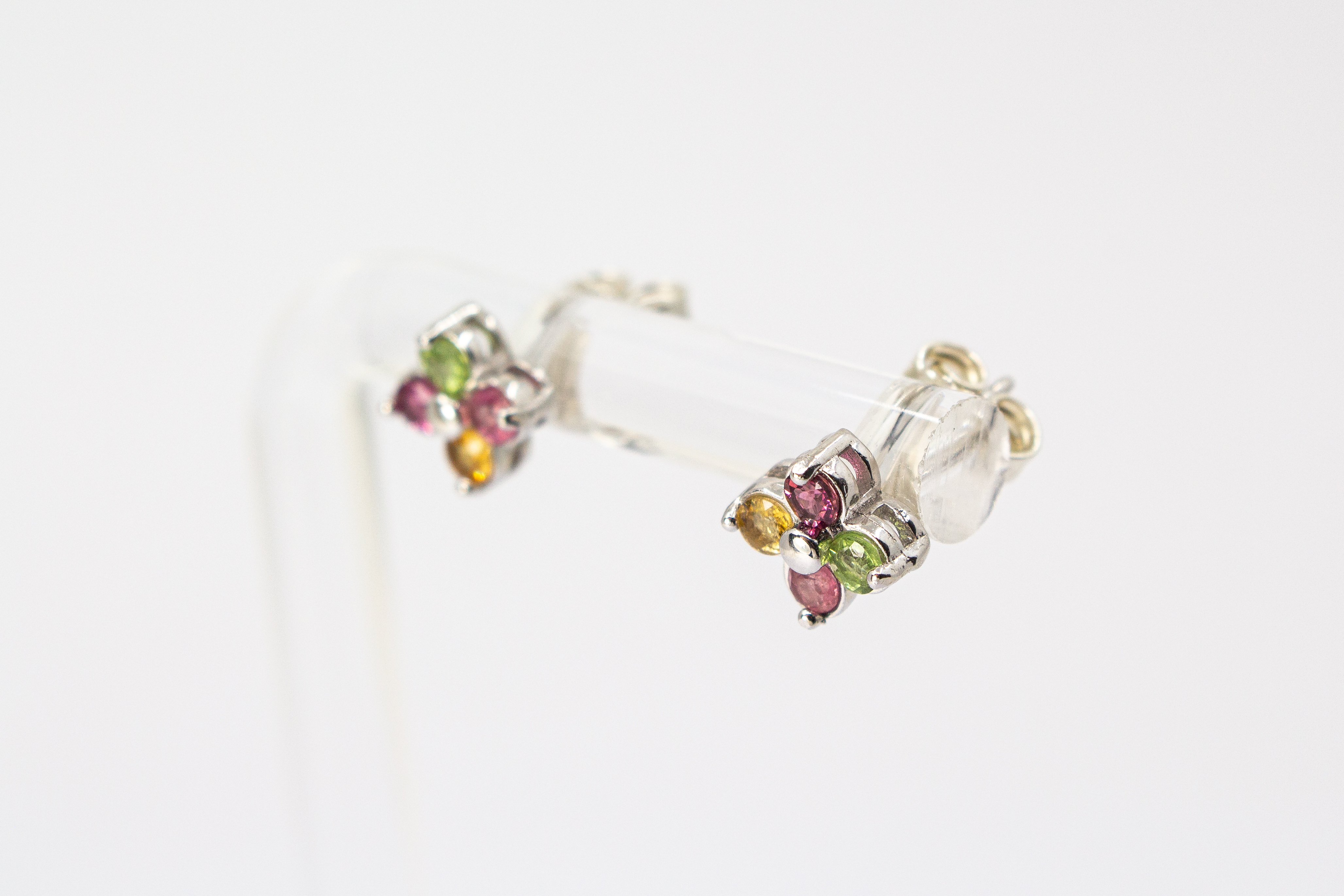 Die filigranen Silber-Ohrstecker „Elfenblüte“ aus der Goldschmiede Regina Kraus an einem transparenten Halter. Die Stecker aus rhodiniertem 925er Sterlingsilber zeigen eine zarte Blütenform, besetzt mit vier bunten Turmalinen in Rosé, Grün und Gelb um ei