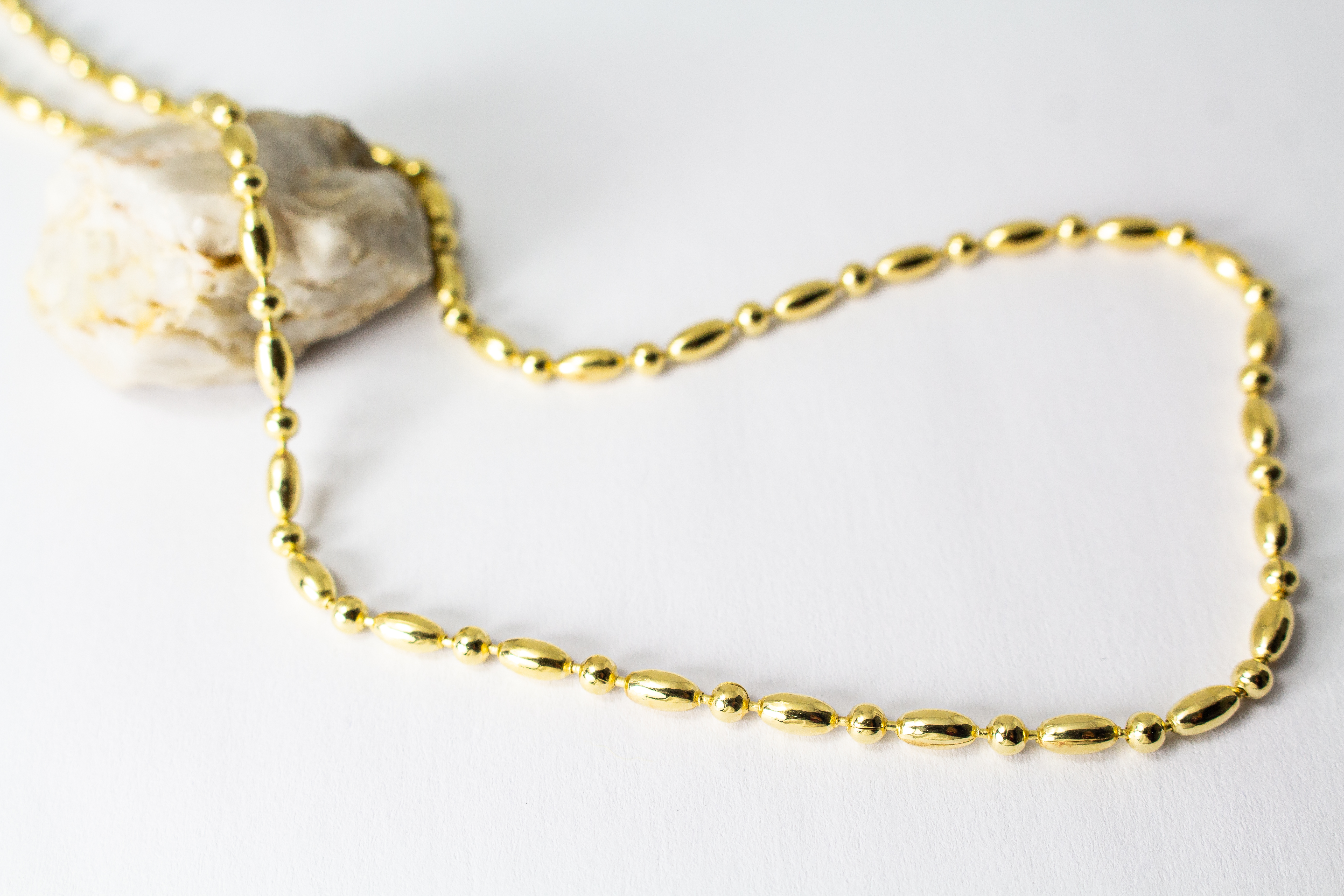 Elegantes, hochwertig vergoldetes Collier aus 925er Sterlingsilber mit einer 20 Mikron Vergoldung, gestaltet in einem rhythmischen Wechsel aus polierten Oliven- und Kugel-Elementen auf hellem Hintergrund, aus dem Schmuck-Onlineshop der Goldschmiede Regina