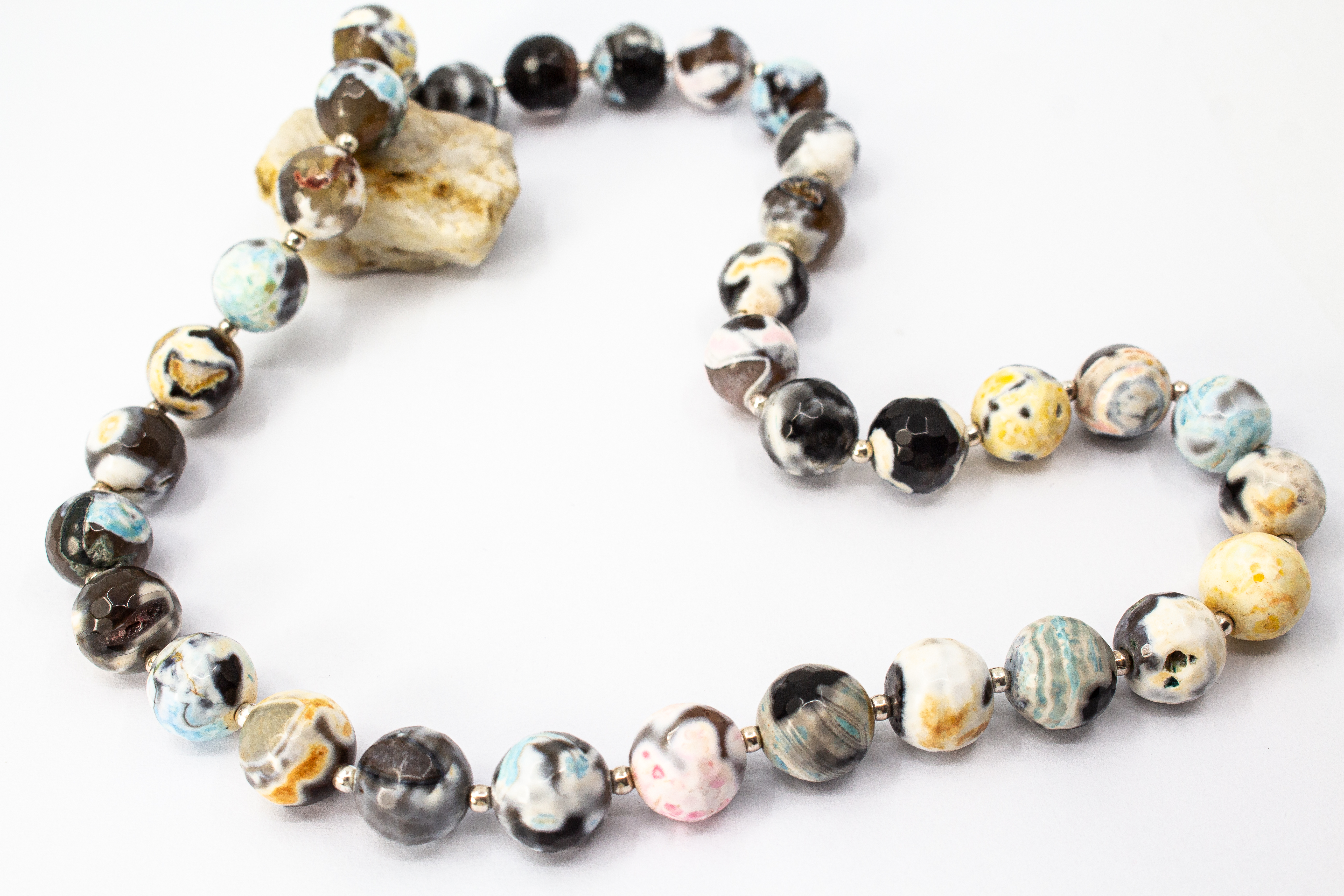Ein handgefertigtes Collier aus bunt gemusterten, runden Feuerachat-Perlen mit kleinen silbernen Zwischenelementen und Magnetschließe