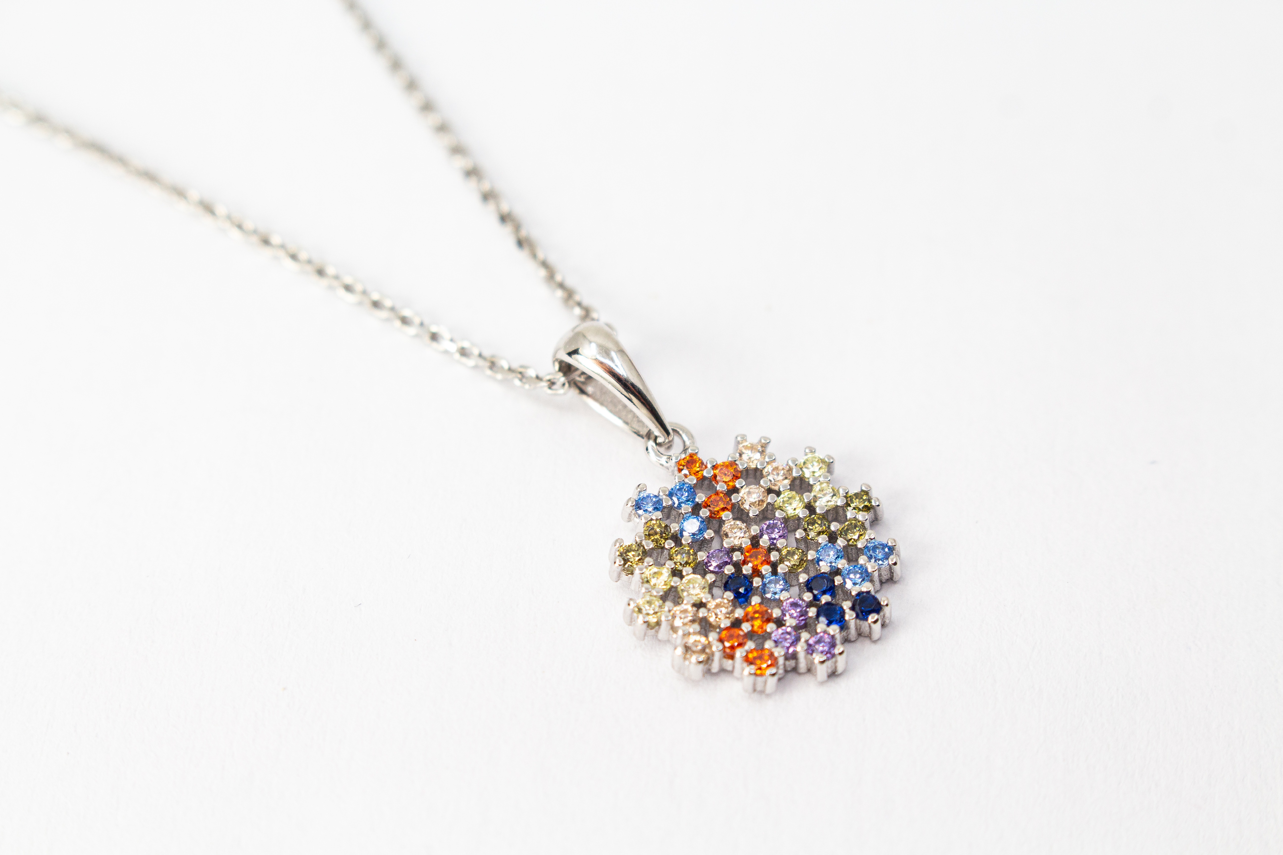 Eine feine Halskette aus rhodiniertem 925er Sterlingsilber von der Goldschmiede Regina Kraus, schräg auf weißem Hintergrund liegend. Der runde Anhänger ist filigran wie ein Mandala oder eine Blüte gestaltet und dicht mit kleinen, bunt funkelnden Zirkonia-