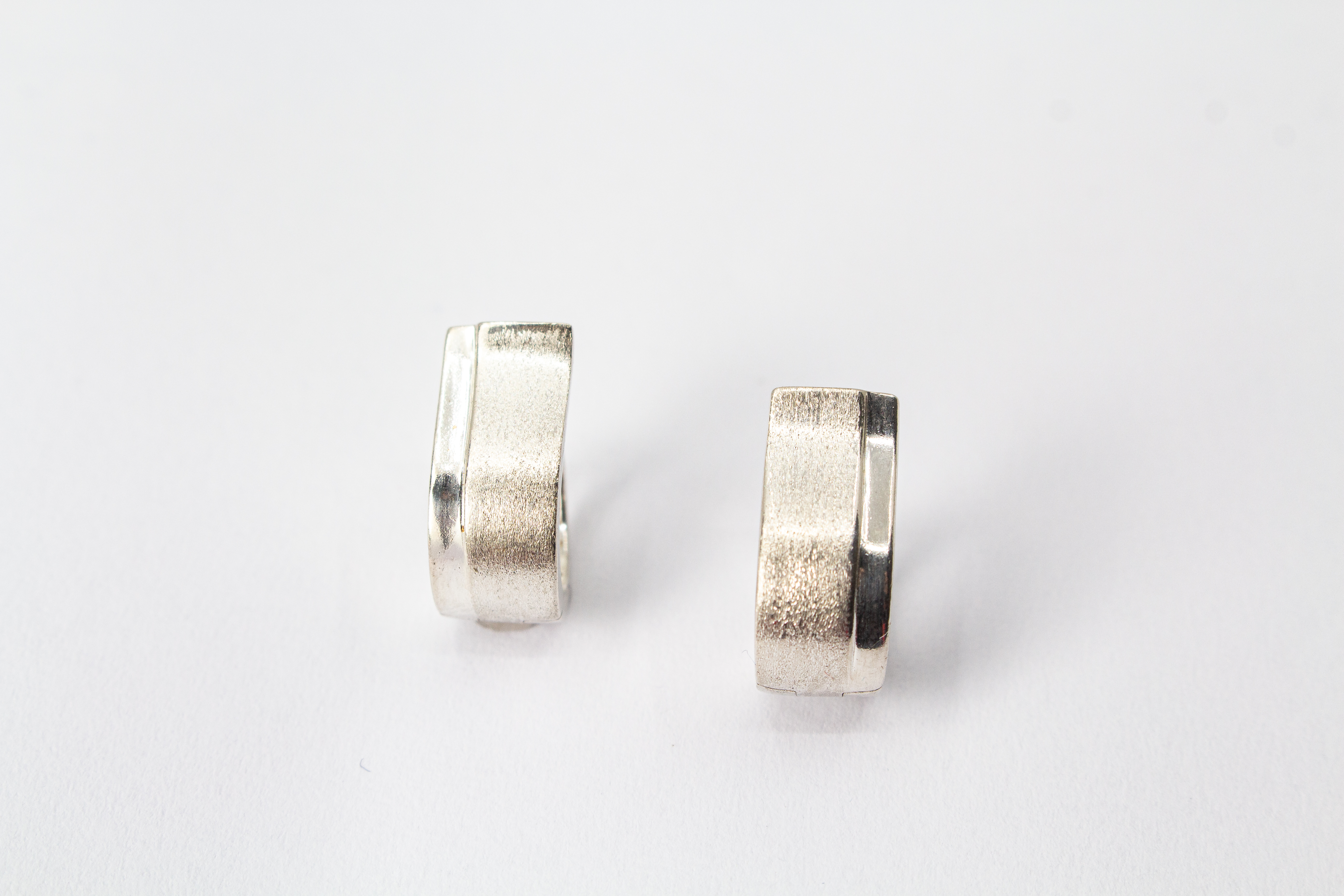 Breite Klappcreolen aus 925er Silber mit einer schwungvoll hochgezogenen, eismattierten Vorderseite und glänzend polierten Kanten im Onlineshop von Goldschmiede Regina Kraus.