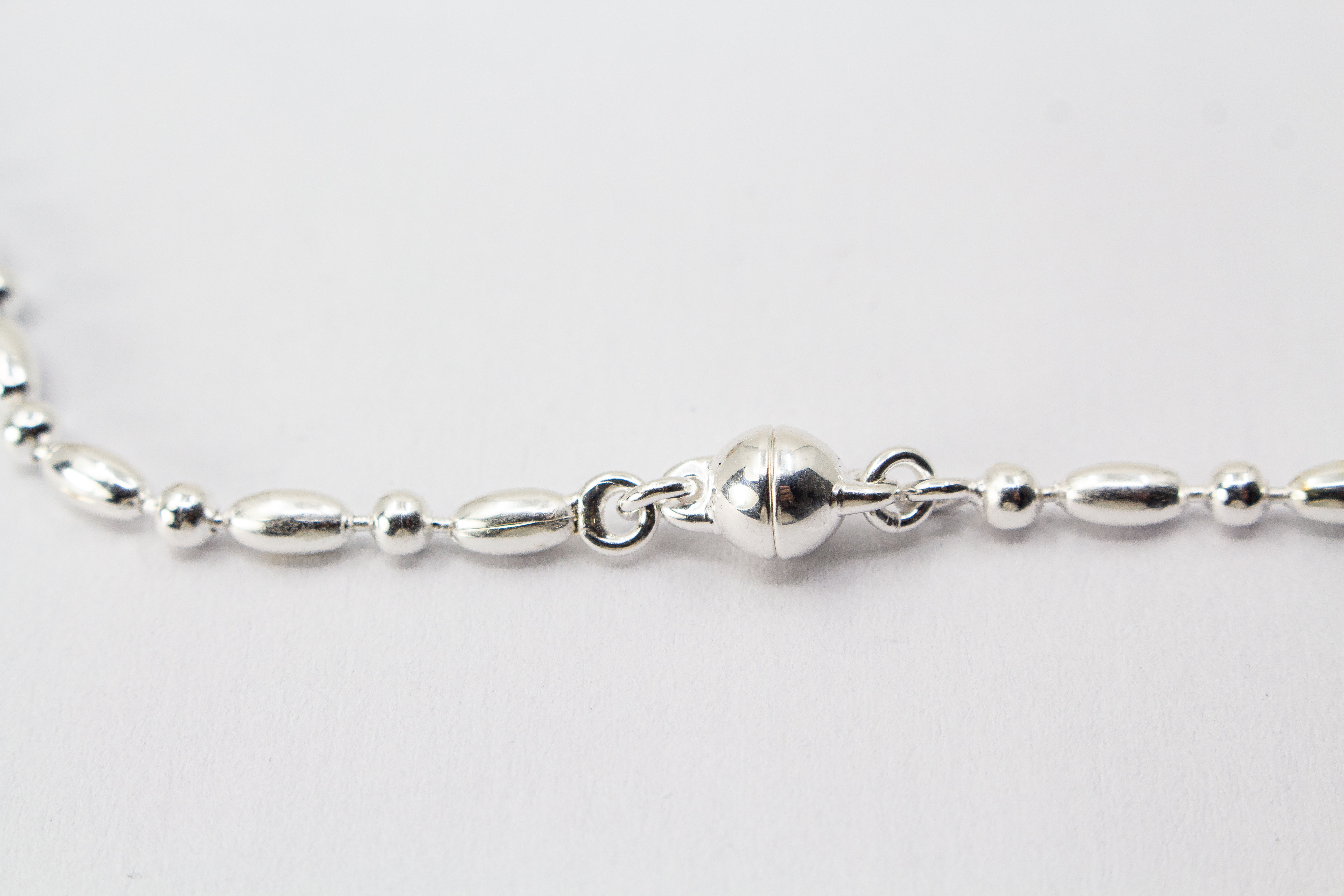 Filigrane Silberkette aus hochglanzpoliertem 925er Sterlingsilber mit einem rhythmischen Wechsel aus Oliven- und Kugel-Elementen auf hellem Untergrund, exklusiv erhältlich im Schmuck-Onlineshop der Goldschmiede Regina Kraus.