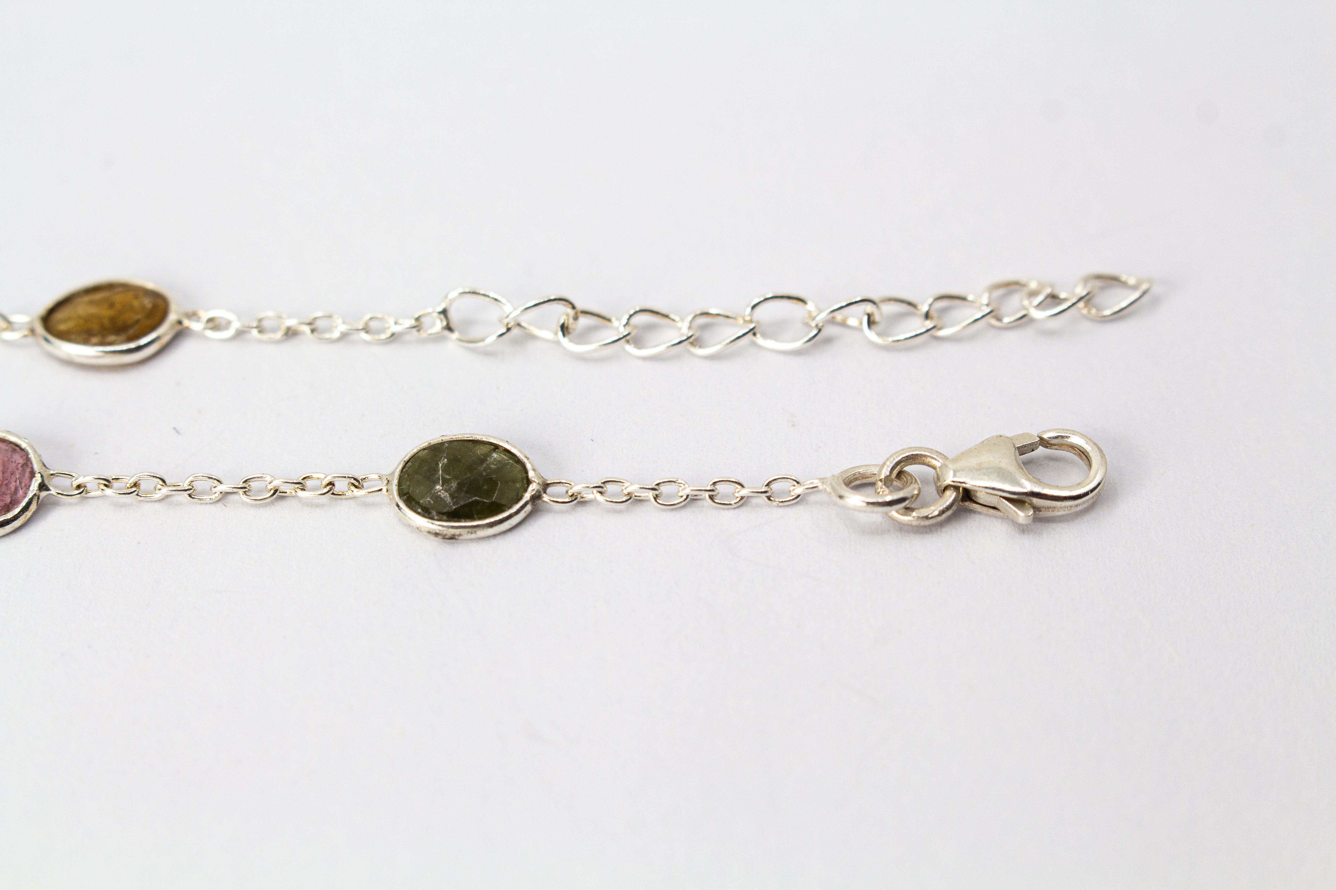 Ein filigranes Armband aus 925 Sterlingsilber von der Goldschmiede Regina Kraus, flach auf weißem Hintergrund arrangiert. In die feine Gliederkette sind sechs verschiedenfarbige, flache Turmaline in ovalen Zargenfassungen eingearbeitet – darunter Gelb-,