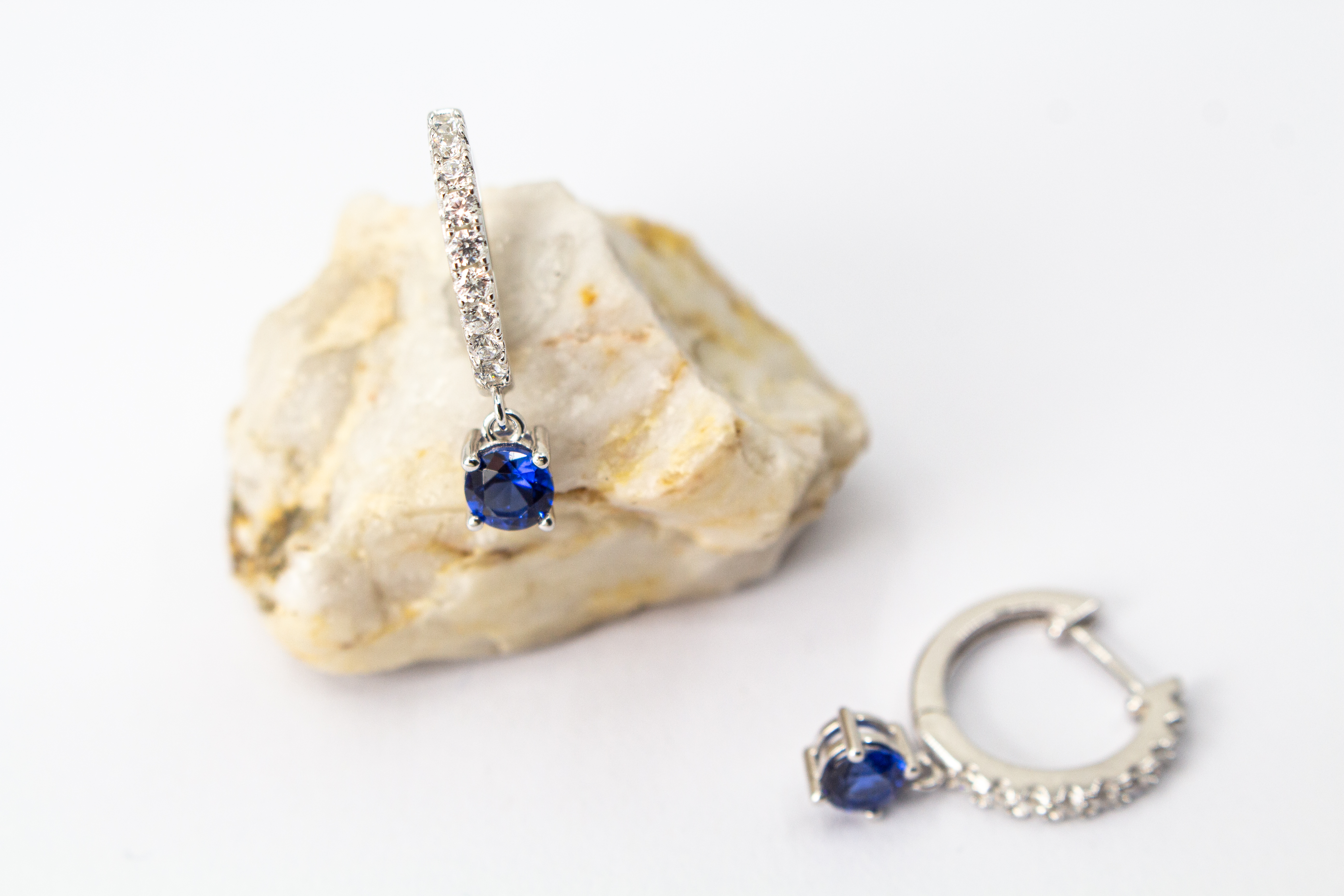 Ein Paar elegante, rhodinierte 925er Silber-Creolen der Goldschmiede Regina Kraus, präsentiert auf einem transparenten Schmuckständer vor weißem Hintergrund. Die Vorderseite der Creolen ist mit einer Reihe kleiner, klarer Zirkonia-Steine besetzt. Am unter