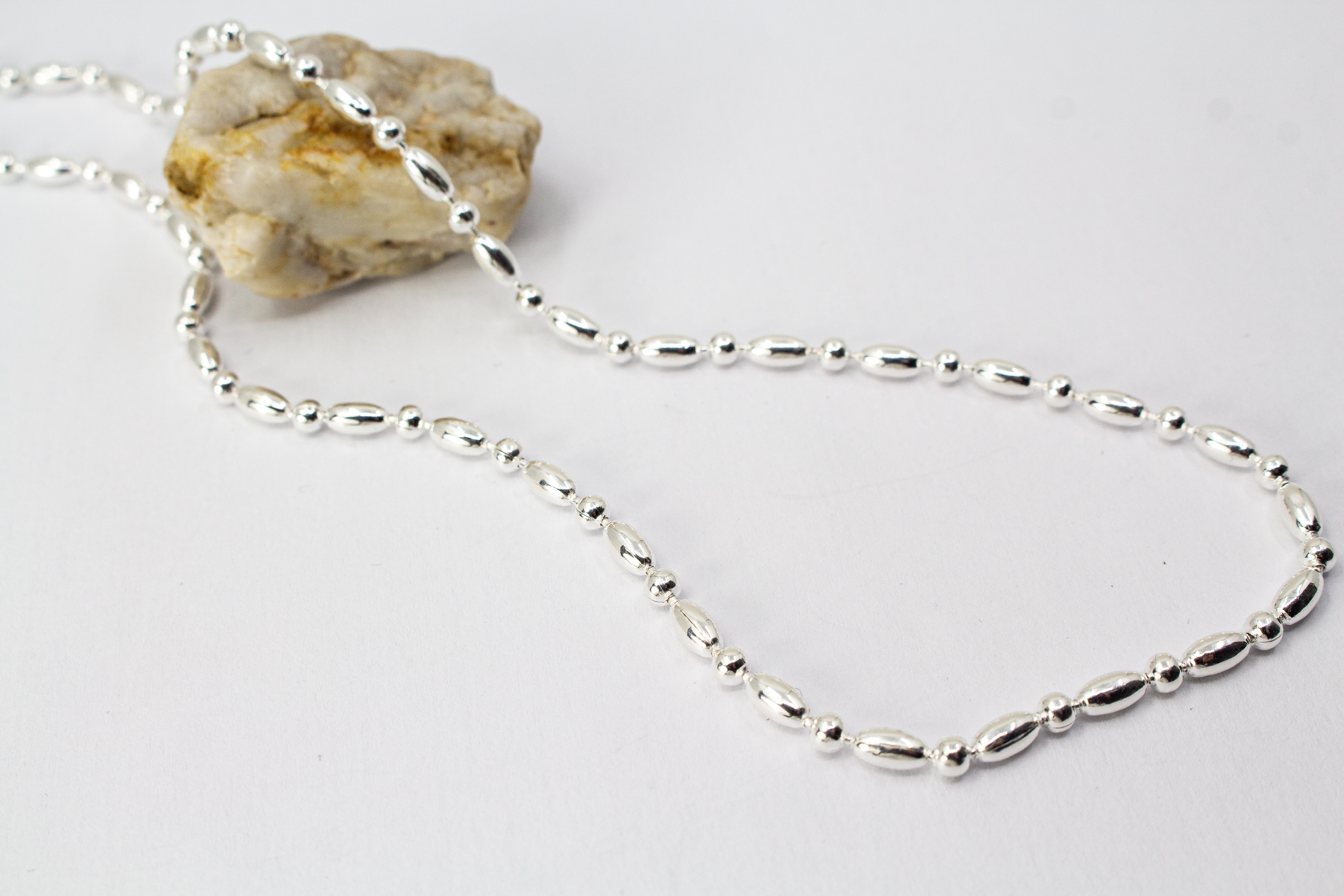 Filigrane Silberkette aus hochglanzpoliertem 925er Sterlingsilber mit einem rhythmischen Wechsel aus Oliven- und Kugel-Elementen auf hellem Untergrund, exklusiv erhältlich im Schmuck-Onlineshop der Goldschmiede Regina Kraus.