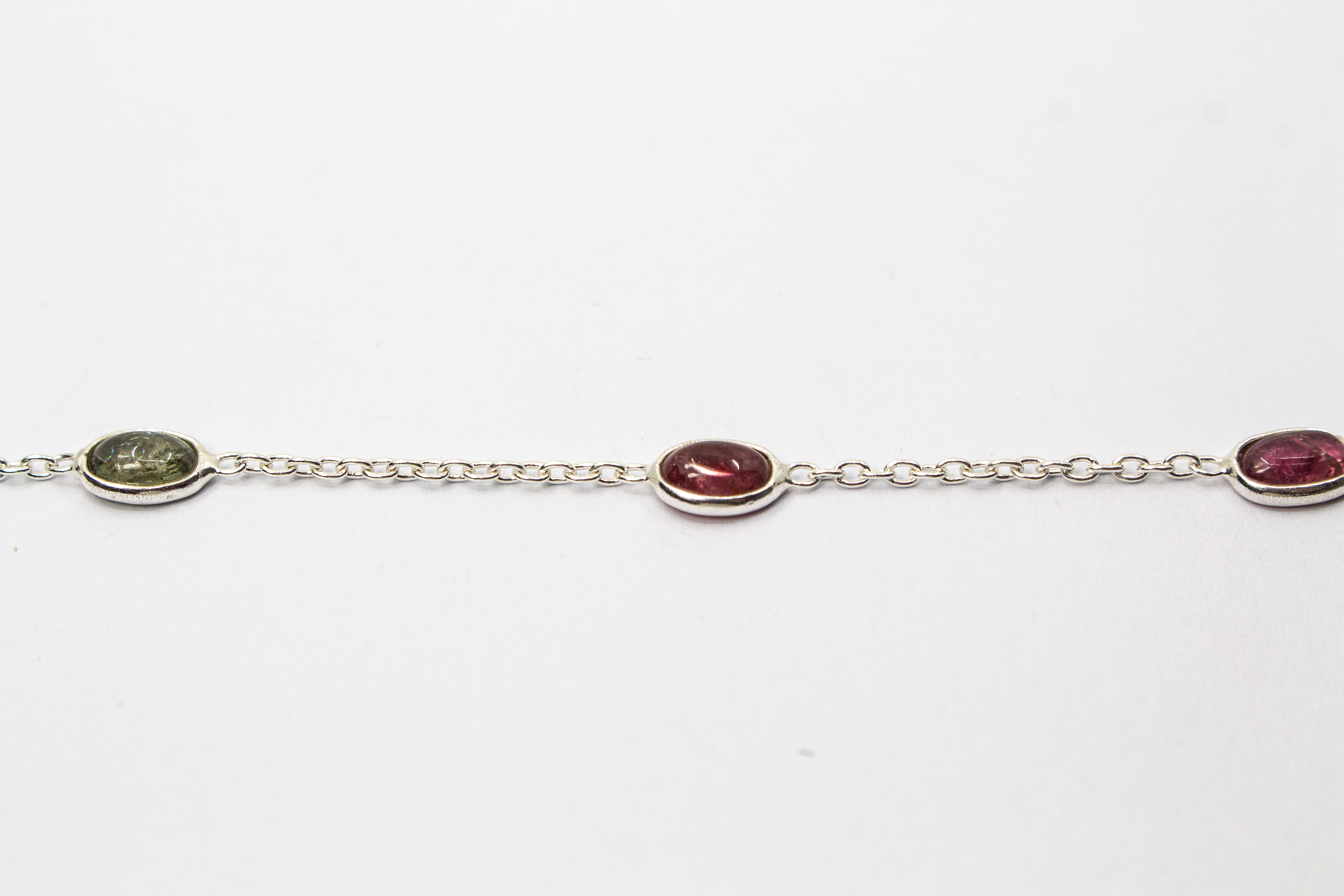 Das filigrane Silber-Armband „Indian Summer“ aus der Goldschmiede Regina Kraus, flach auf weißem Untergrund arrangiert. Die feine Kette aus rhodiniertem 925er Sterlingsilber verbindet fünf ovale Turmalin-Cabochons in den warmen Farben Weinrot, Moosgrün, R