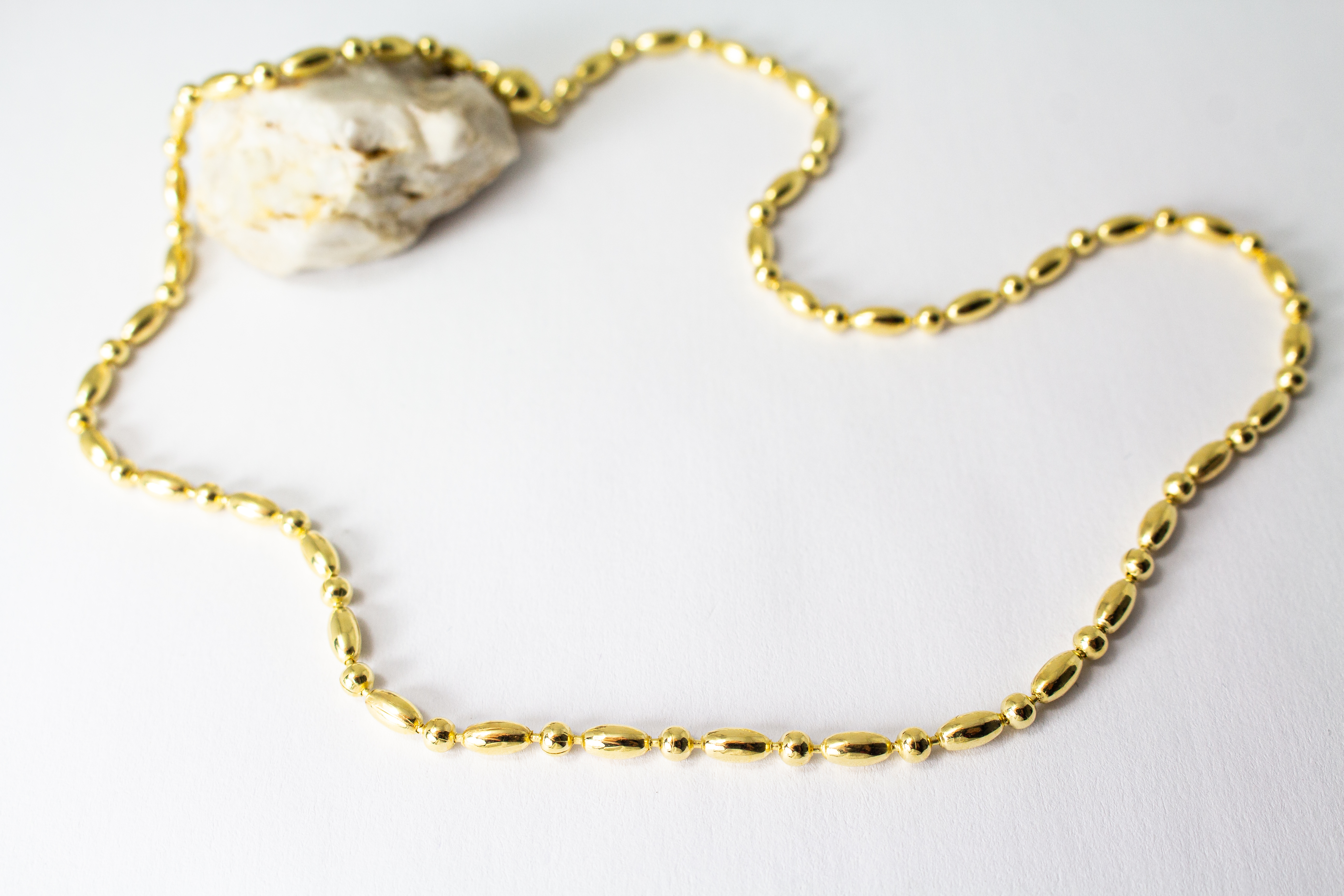 Elegantes, hochwertig vergoldetes Collier aus 925er Sterlingsilber mit einer 20 Mikron Vergoldung, gestaltet in einem rhythmischen Wechsel aus polierten Oliven- und Kugel-Elementen auf hellem Hintergrund, aus dem Schmuck-Onlineshop der Goldschmiede Regina