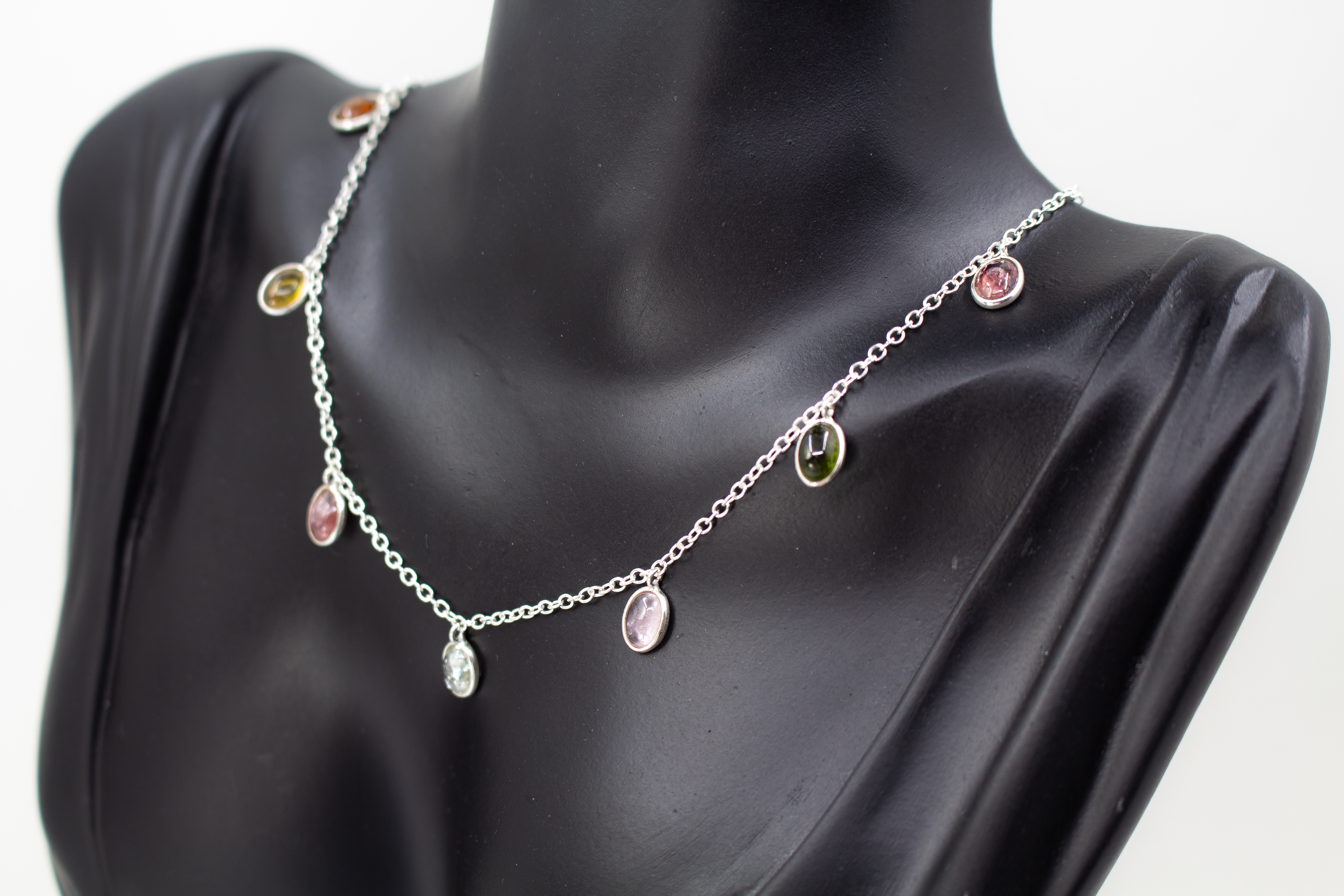 Die filigrane 925er Silber-Halskette „Kaleidoskop der Natur“ aus der Goldschmiede Regina Kraus, spiralförmig auf hellem Grund arrangiert. Das Design besticht durch ein buntes Farbspiel aus elf facettierten, ovalen Turmalinen in zarten Silberfassungen, die
