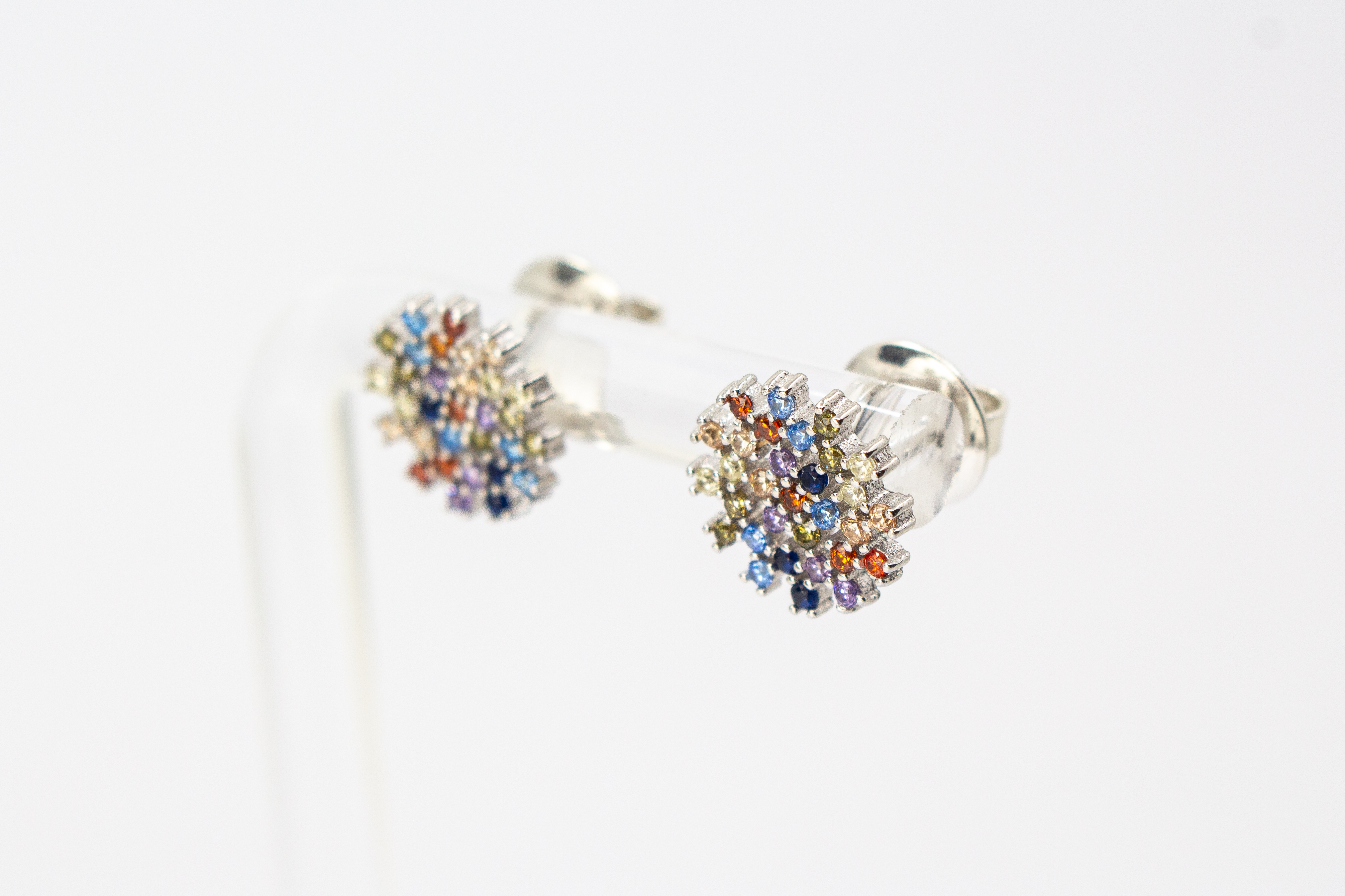 Die filigranen 925er Silber-Ohrstecker „Fleur de Lumière“ aus der Goldschmiede Regina Kraus, präsentiert auf einem transparenten Schmuckständer. Das florale Design erinnert an eine funkelnde Lichtblume und ist kunstvoll mit kleinen, bunt strahlenden Zirk