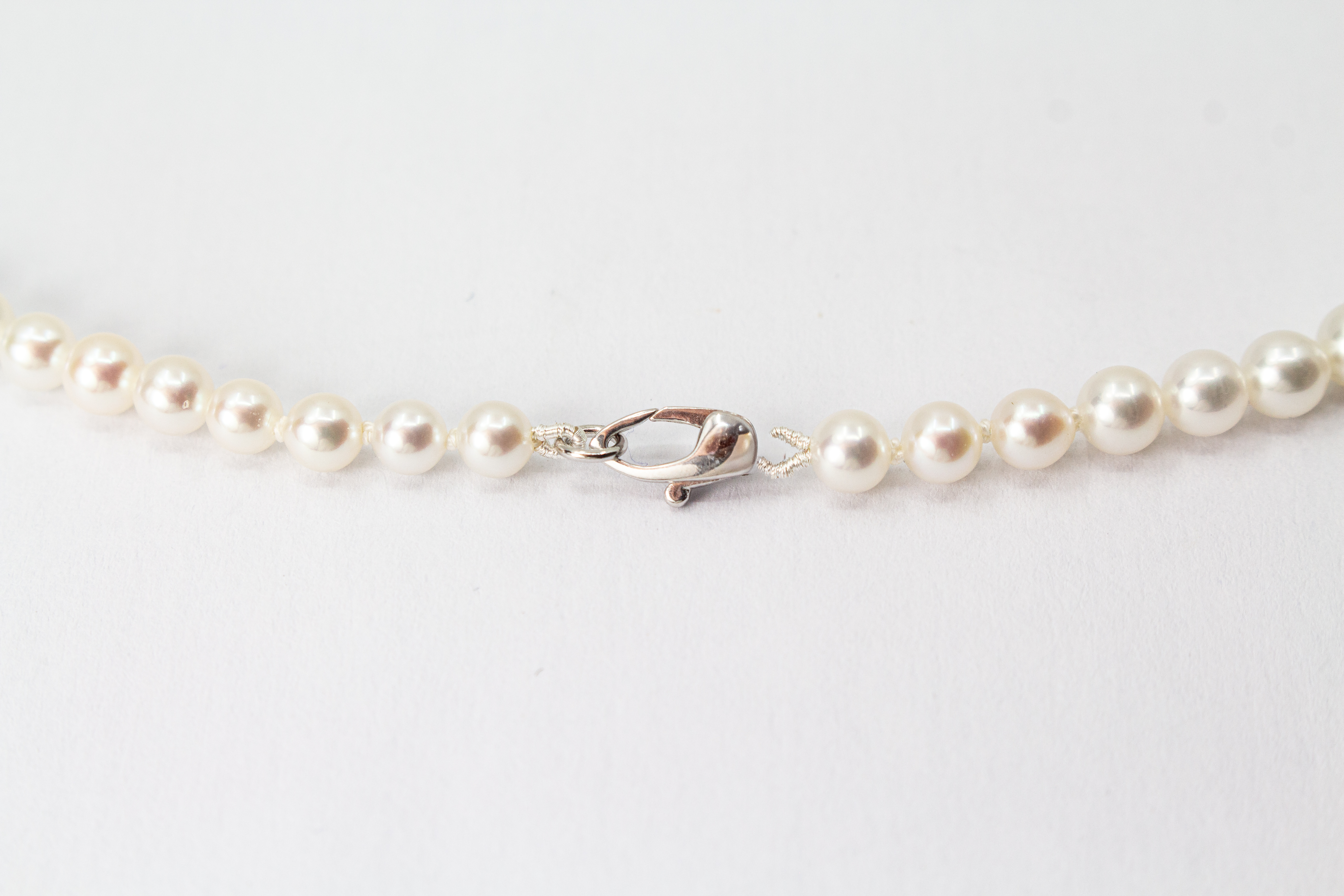Eine klassische Süßwasserzuchtperlenkette von der Goldschmiede Regina Kraus, elegant geschwungen auf weißem Hintergrund ausgelegt. Die runden Perlen weisen einen zarten, cremeweißen Lüster auf und sind im harmonischen Verlauf angeordnet, wobei die größte