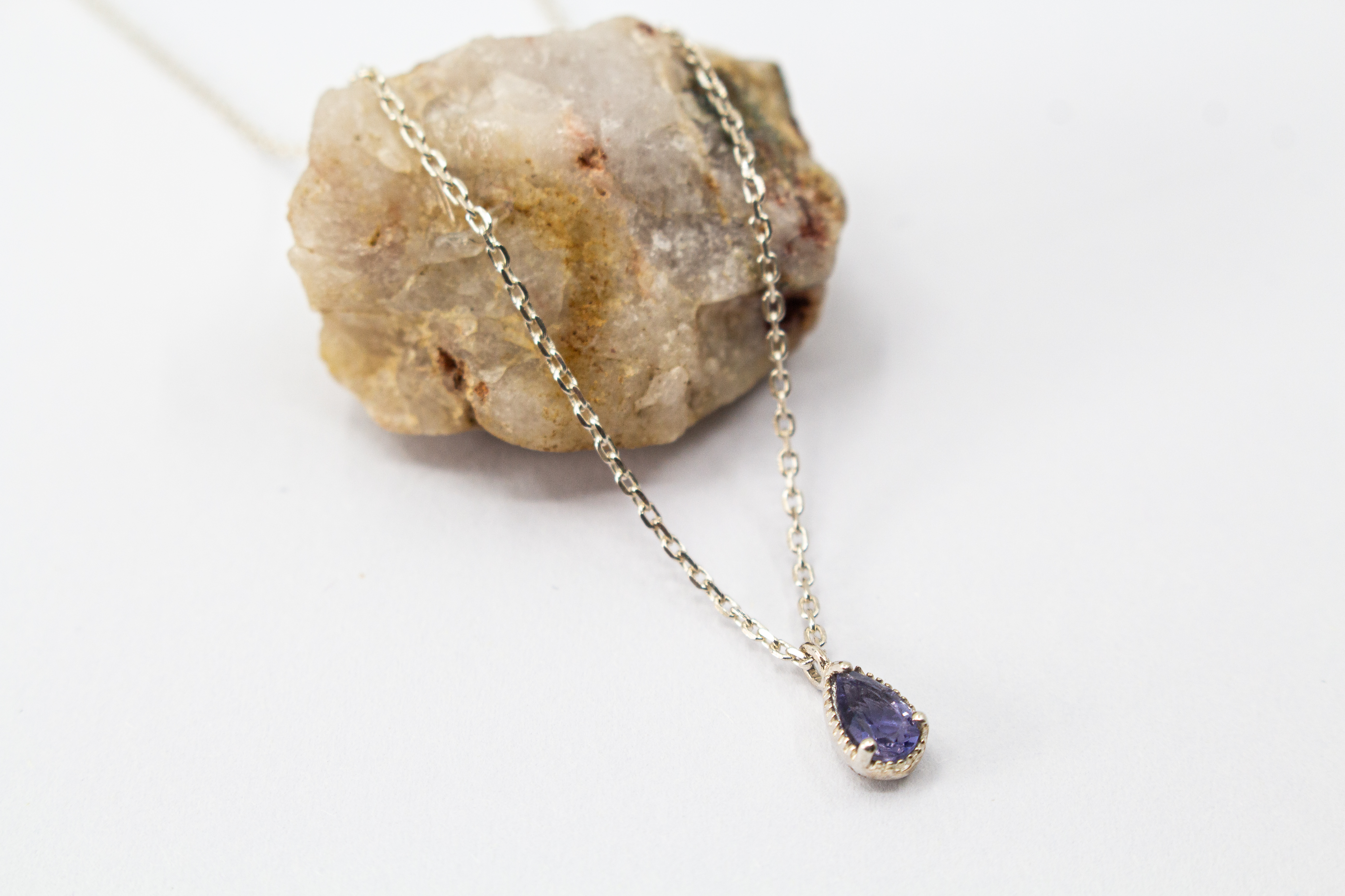Filigrane Halskette aus 925 Sterling Silber mit einem kleinen, tropfenförmigen, facettierten blau-violetten Iolith-Edelstein in einer fein verzierten Fassung aus dem Online-Shop der Goldschmiede Regina Kraus.