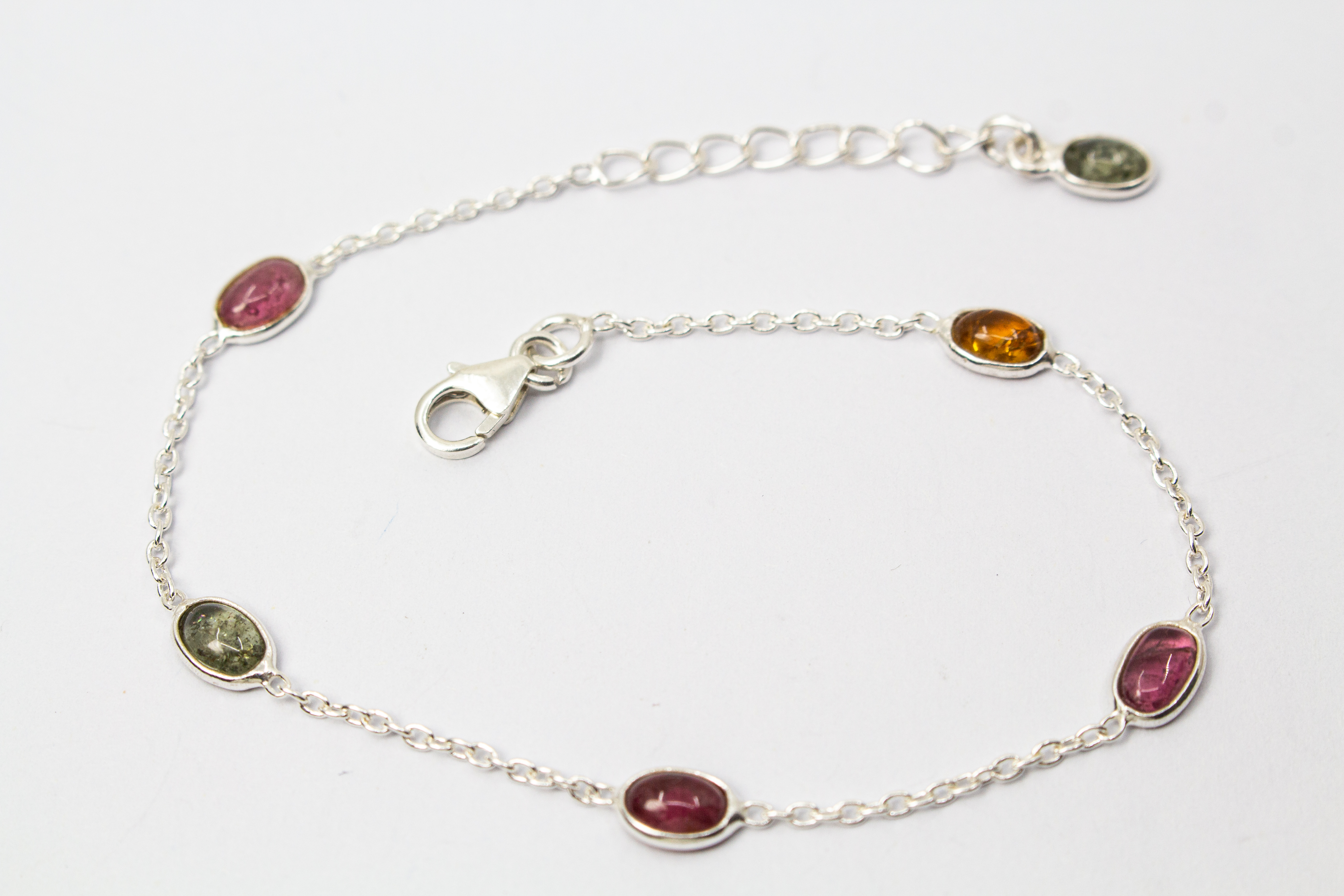 Das filigrane Silber-Armband „Indian Summer“ aus der Goldschmiede Regina Kraus, flach auf weißem Untergrund arrangiert. Die feine Kette aus rhodiniertem 925er Sterlingsilber verbindet fünf ovale Turmalin-Cabochons in den warmen Farben Weinrot, Moosgrün, R