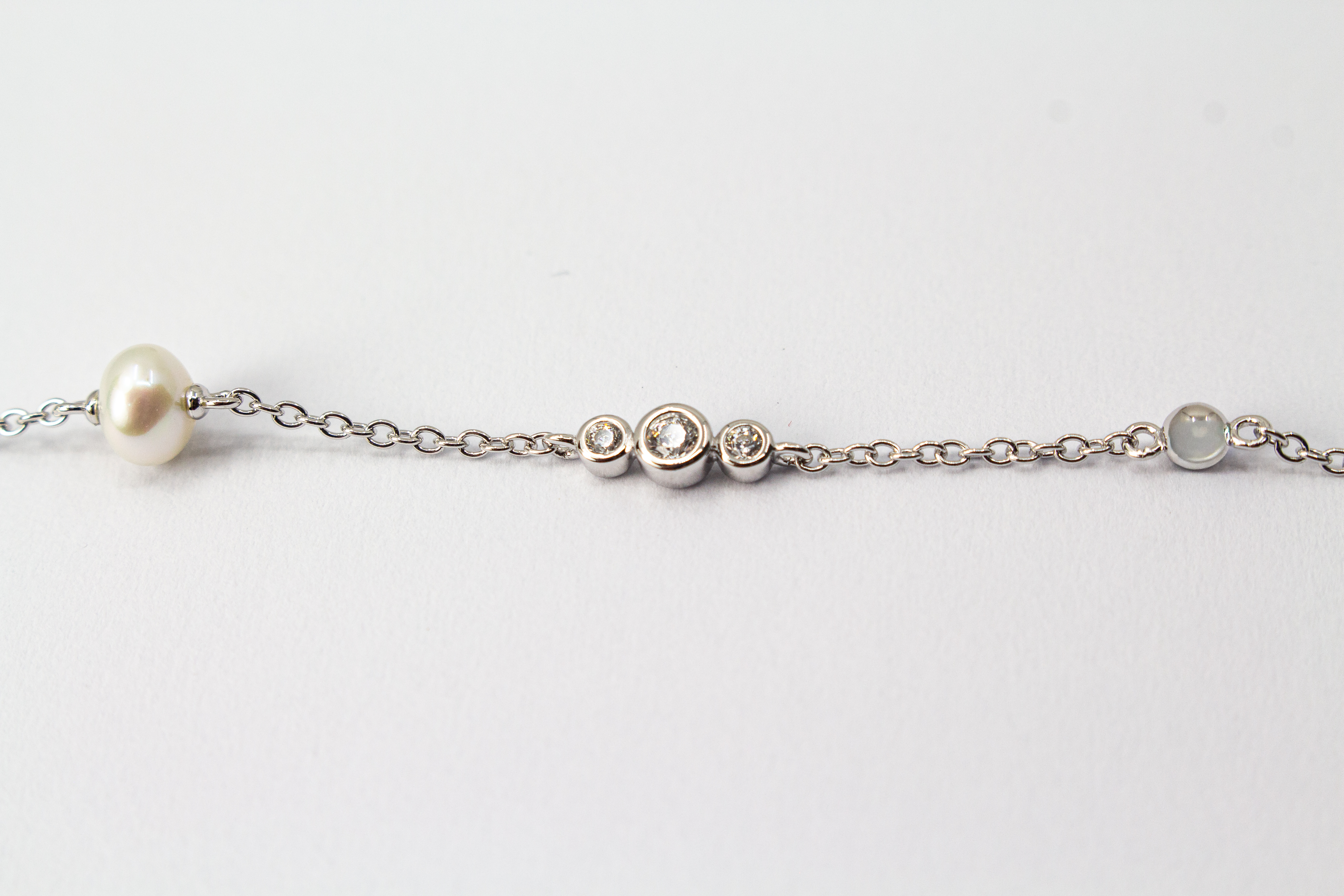 Zartes Armkettchen 'Pearl and Glint' aus rhodiniertem 925er Sterlingsilber mit einer zentralen Süßwasserzuchtperle und seitlichen Zirkonia-Einsätzen,