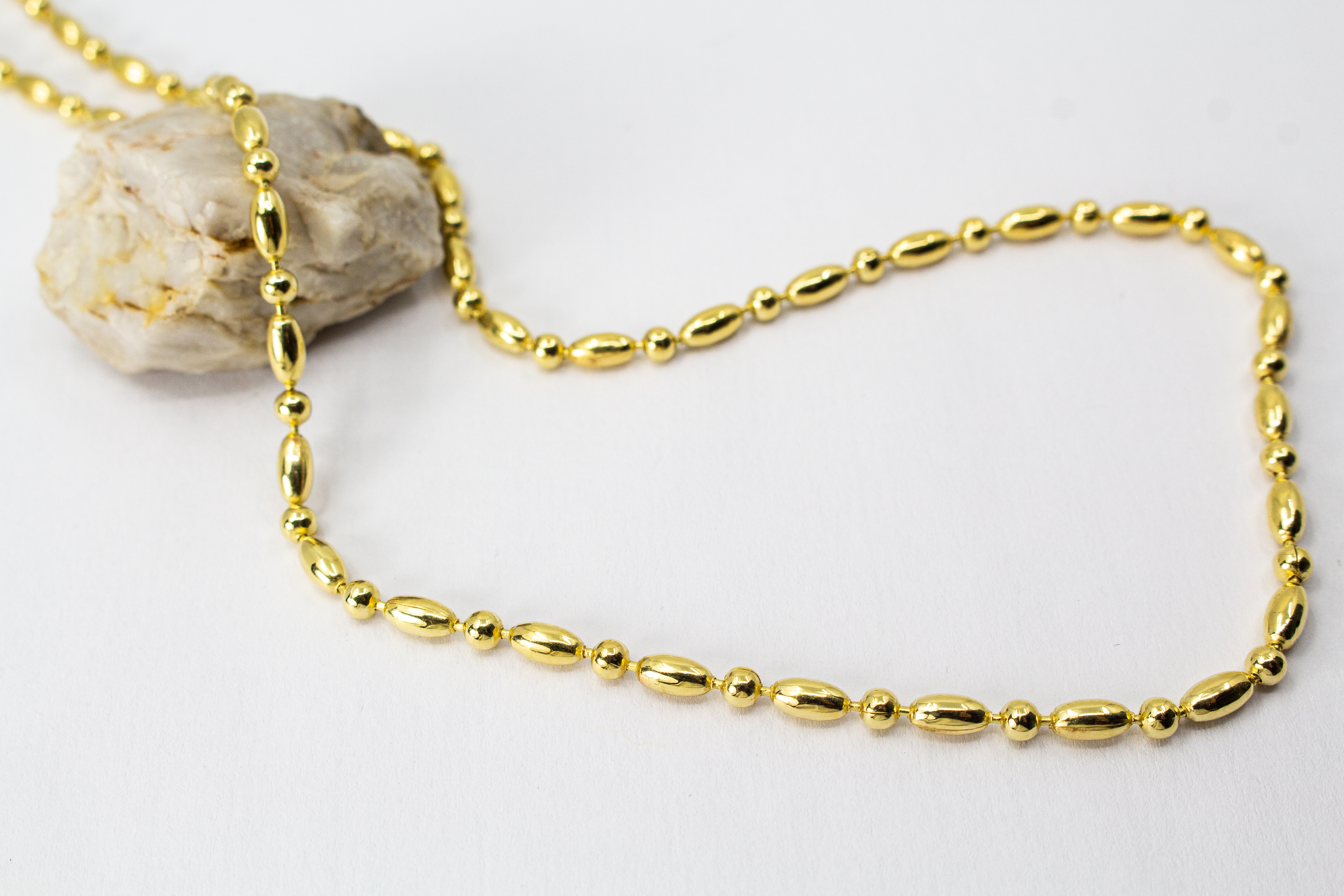 Elegantes, hochwertig vergoldetes Collier aus 925er Sterlingsilber mit einer 20 Mikron Vergoldung, gestaltet in einem rhythmischen Wechsel aus polierten Oliven- und Kugel-Elementen auf hellem Hintergrund, aus dem Schmuck-Onlineshop der Goldschmiede Regina