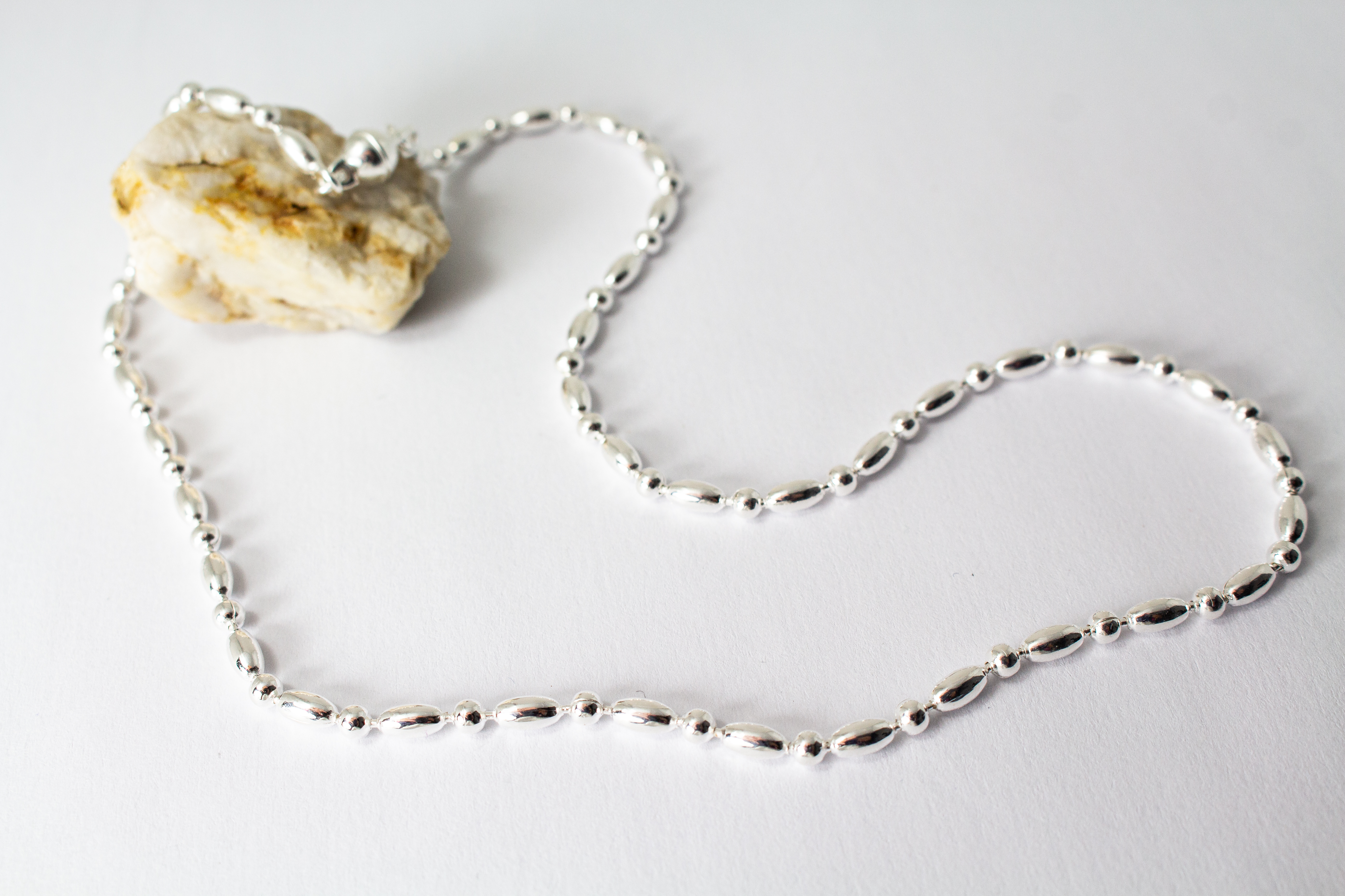 Filigrane Silberkette aus hochglanzpoliertem 925er Sterlingsilber mit einem rhythmischen Wechsel aus Oliven- und Kugel-Elementen auf hellem Untergrund, exklusiv erhältlich im Schmuck-Onlineshop der Goldschmiede Regina Kraus.