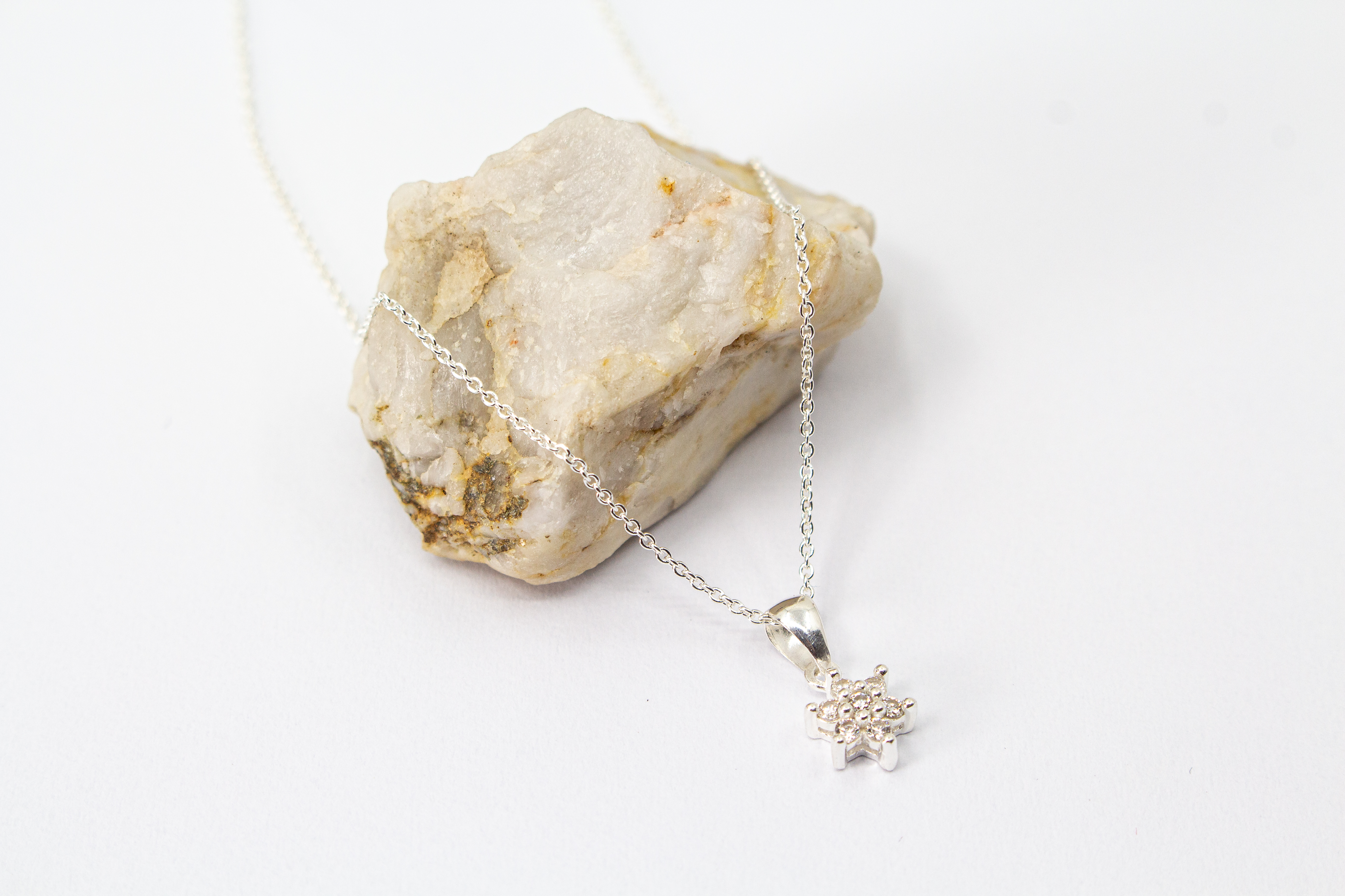 Filigrane Halskette aus 925er Sterling-Silber mit einem stern- oder blütenförmigen Anhänger, der mit funkelnden Zirkonia-Kristallen besetzt ist, präsentiert auf einem hellen Naturstein – exklusiver Schmuck von der Goldschmiede Regina Kraus.