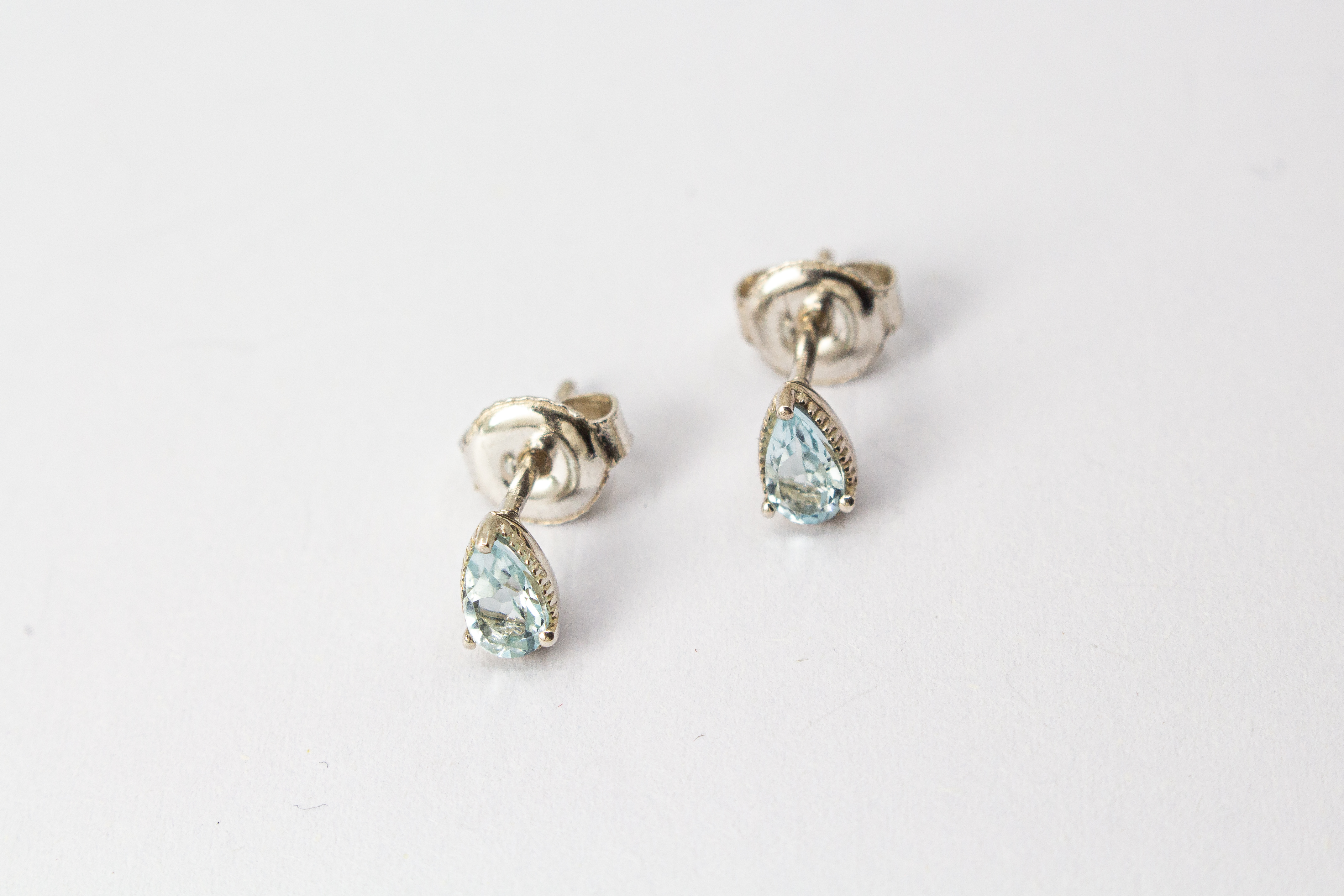 filigrane Ohrstecker aus glänzendem 925 Sterling Silber mit kleinen, tropfenförmigen, hellblauen Topas-Edelsteinen in einer fein verzierten Krappenfassung aus dem Online-Shop der Goldschmiede Regina Kraus.