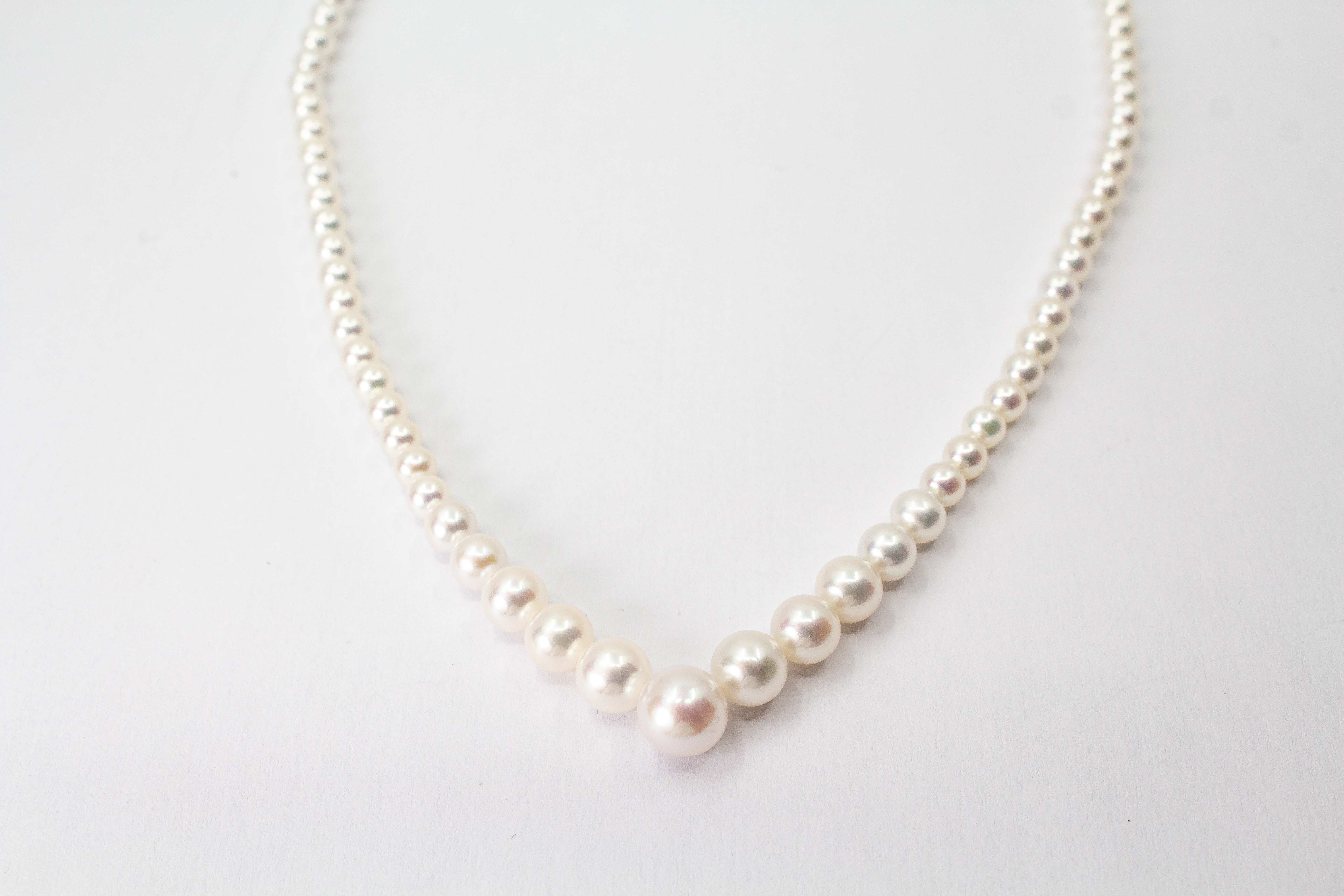 Eine klassische Süßwasserzuchtperlenkette von der Goldschmiede Regina Kraus, elegant geschwungen auf weißem Hintergrund ausgelegt. Die runden Perlen weisen einen zarten, cremeweißen Lüster auf und sind im harmonischen Verlauf angeordnet, wobei die größte