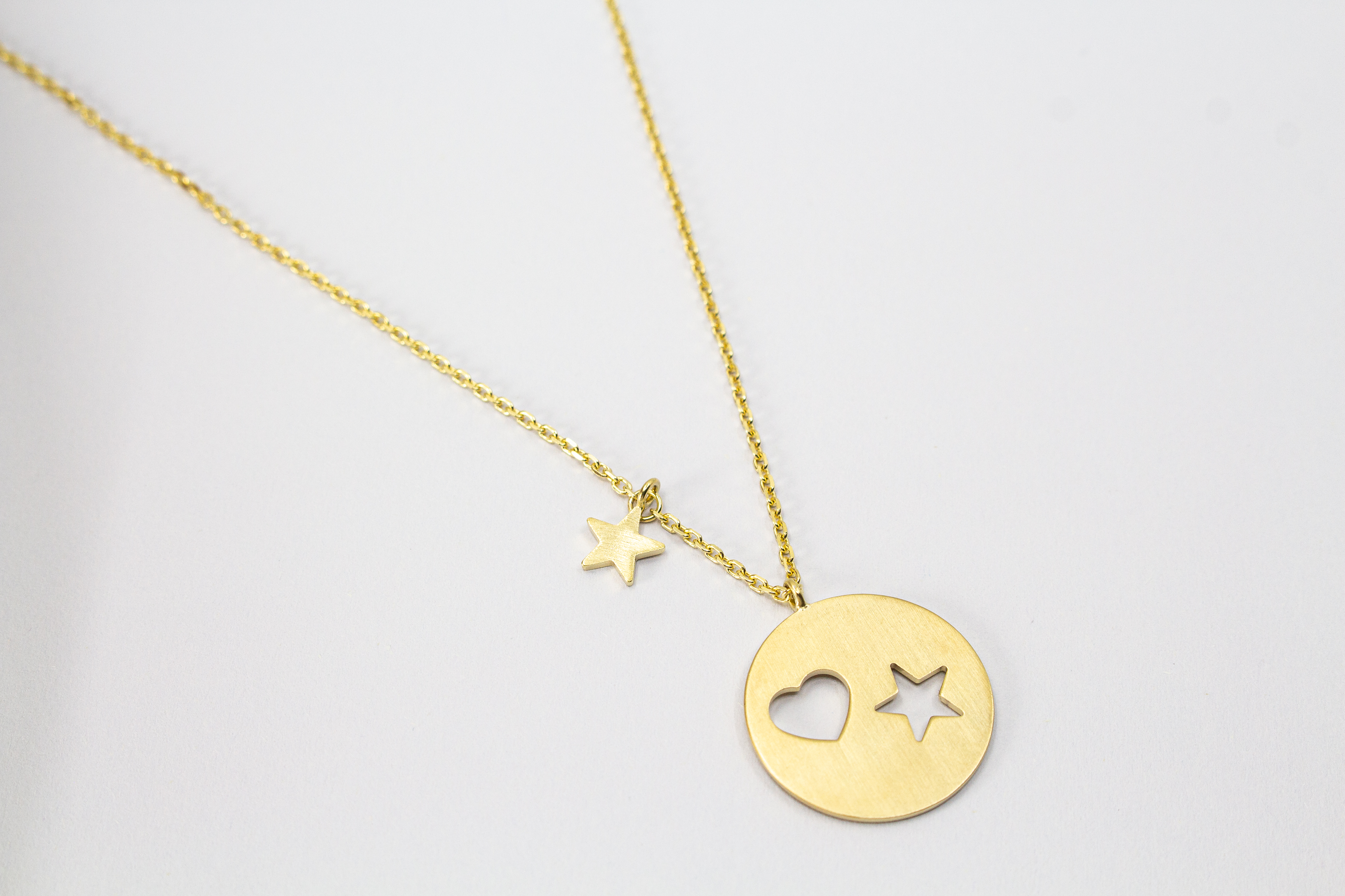 Collier „Sternenliebe“ aus vergoldetem 925er Sterlingsilber mit rundem Anhänger, Herz- und Sternmotiv sowie zusätzlichem Sternanhänger.