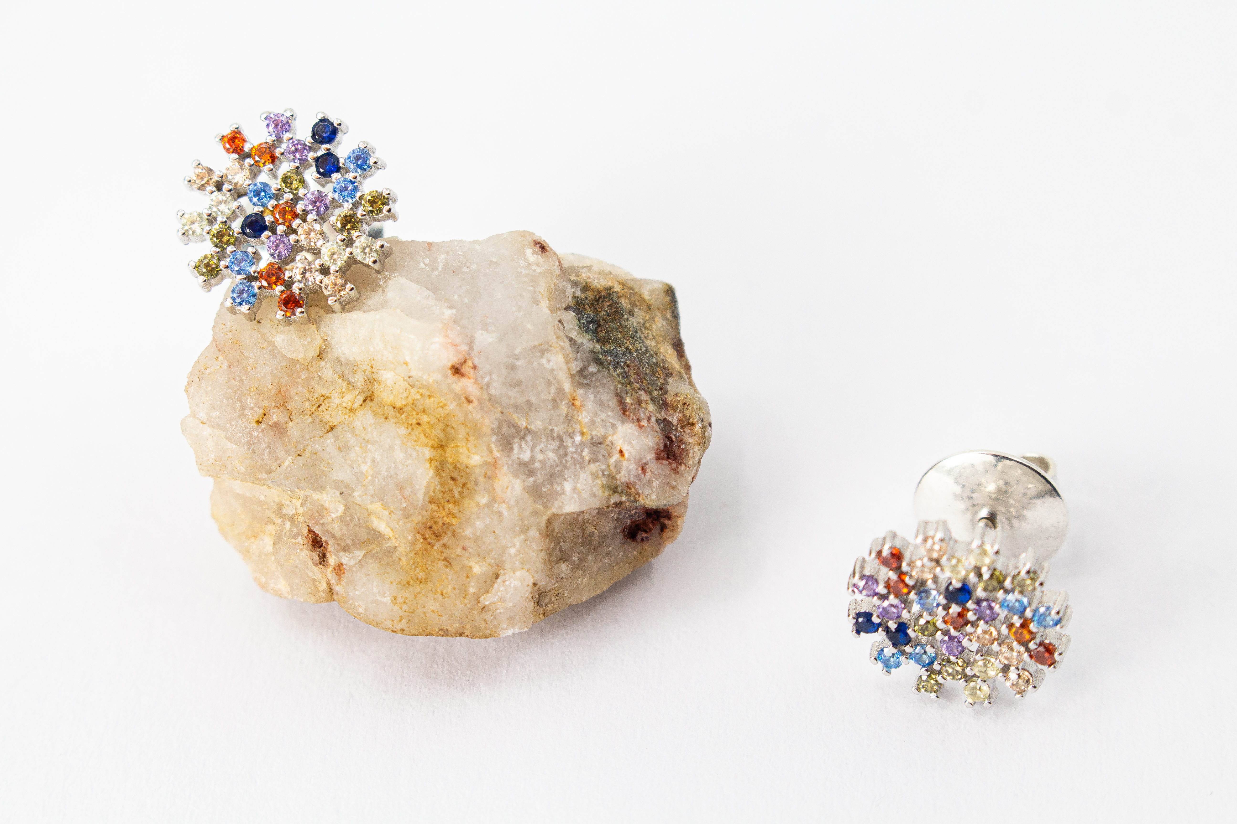 Die filigranen 925er Silber-Ohrstecker „Fleur de Lumière“ aus der Goldschmiede Regina Kraus, präsentiert auf einem transparenten Schmuckständer. Das florale Design erinnert an eine funkelnde Lichtblume und ist kunstvoll mit kleinen, bunt strahlenden Zirk