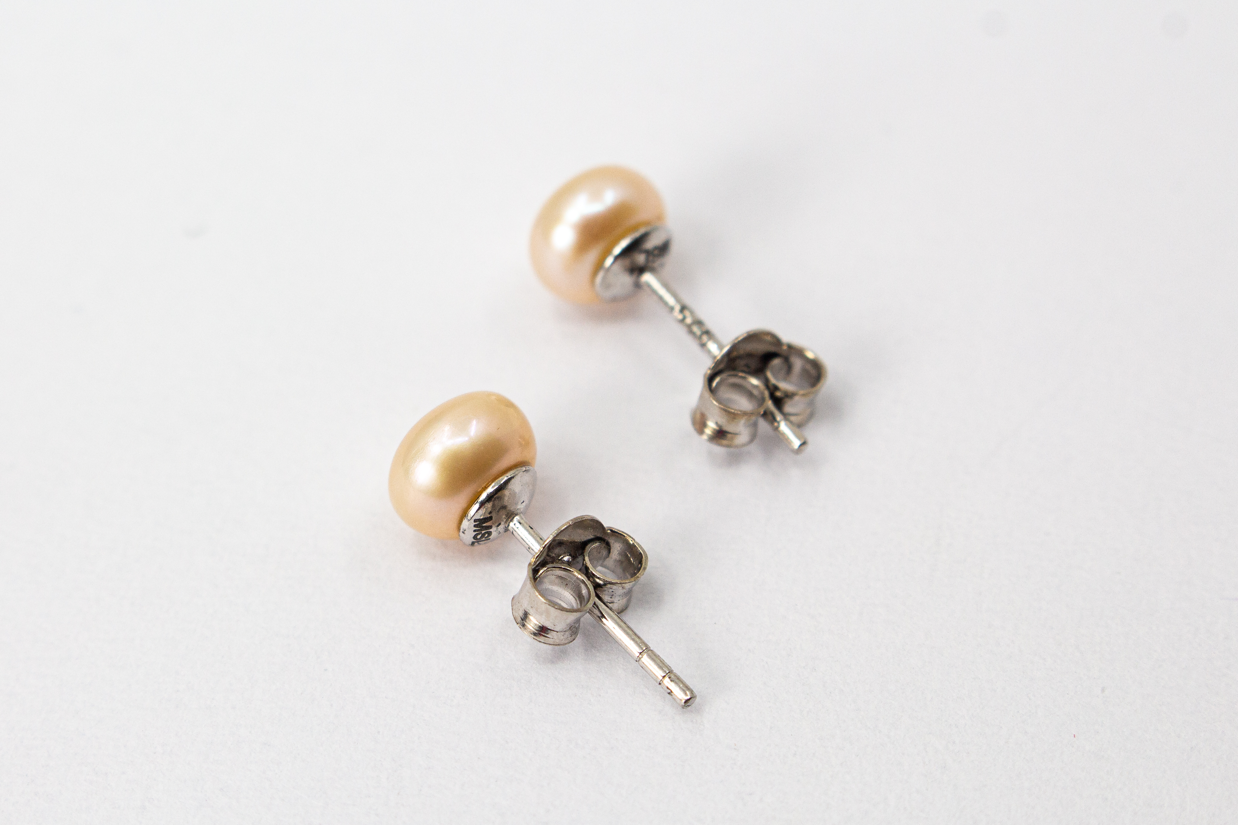 Ein Paar klassische Damen-Ohrstecker aus poliertem 925 Sterlingsilber mit je einer runden, lachsfarbenen Süßwasserzuchtperle, präsentiert von der Goldschmiede Regina Kraus.