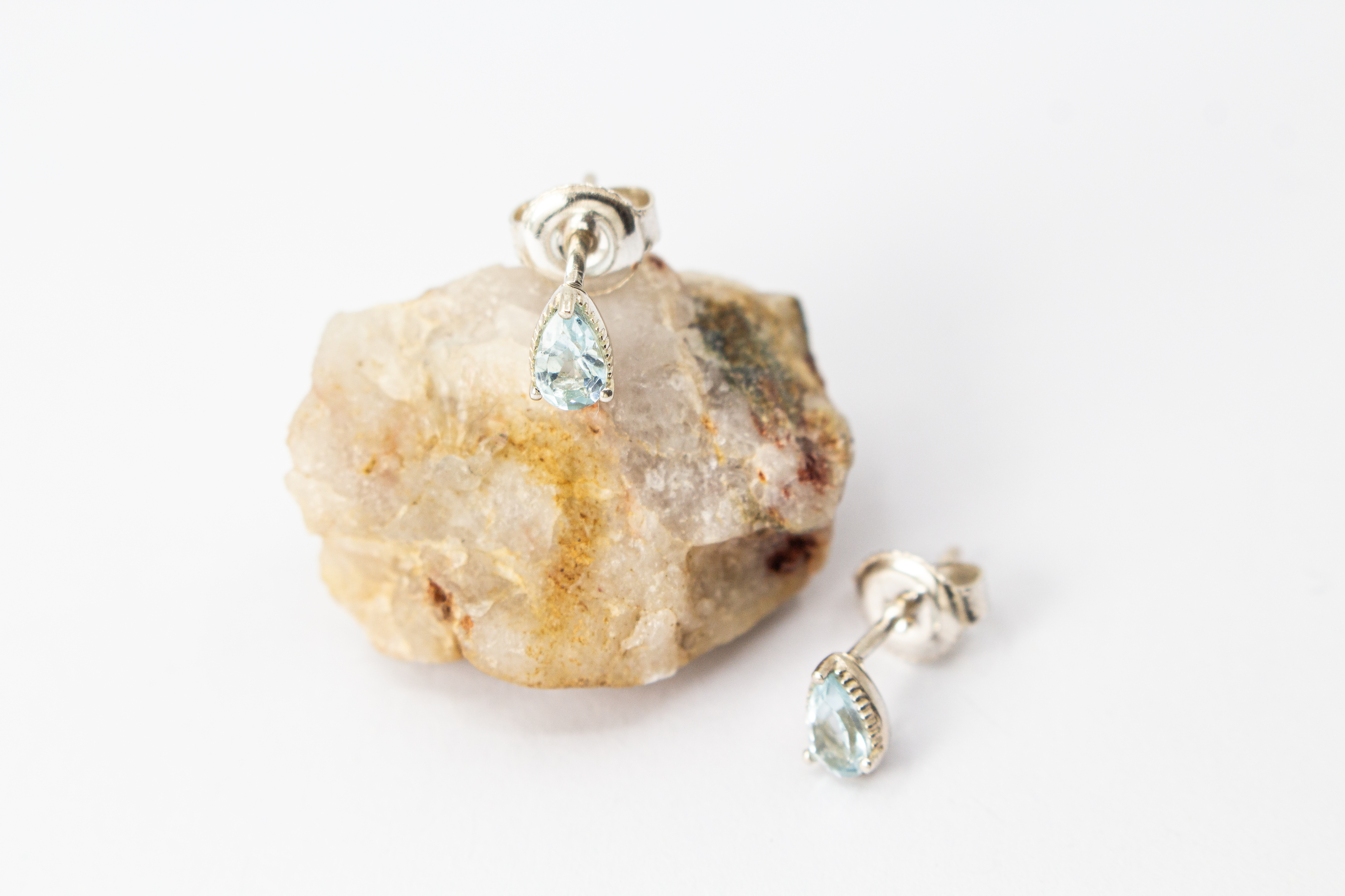 filigrane Ohrstecker aus glänzendem 925 Sterling Silber mit kleinen, tropfenförmigen, hellblauen Topas-Edelsteinen in einer fein verzierten Krappenfassung aus dem Online-Shop der Goldschmiede Regina Kraus.