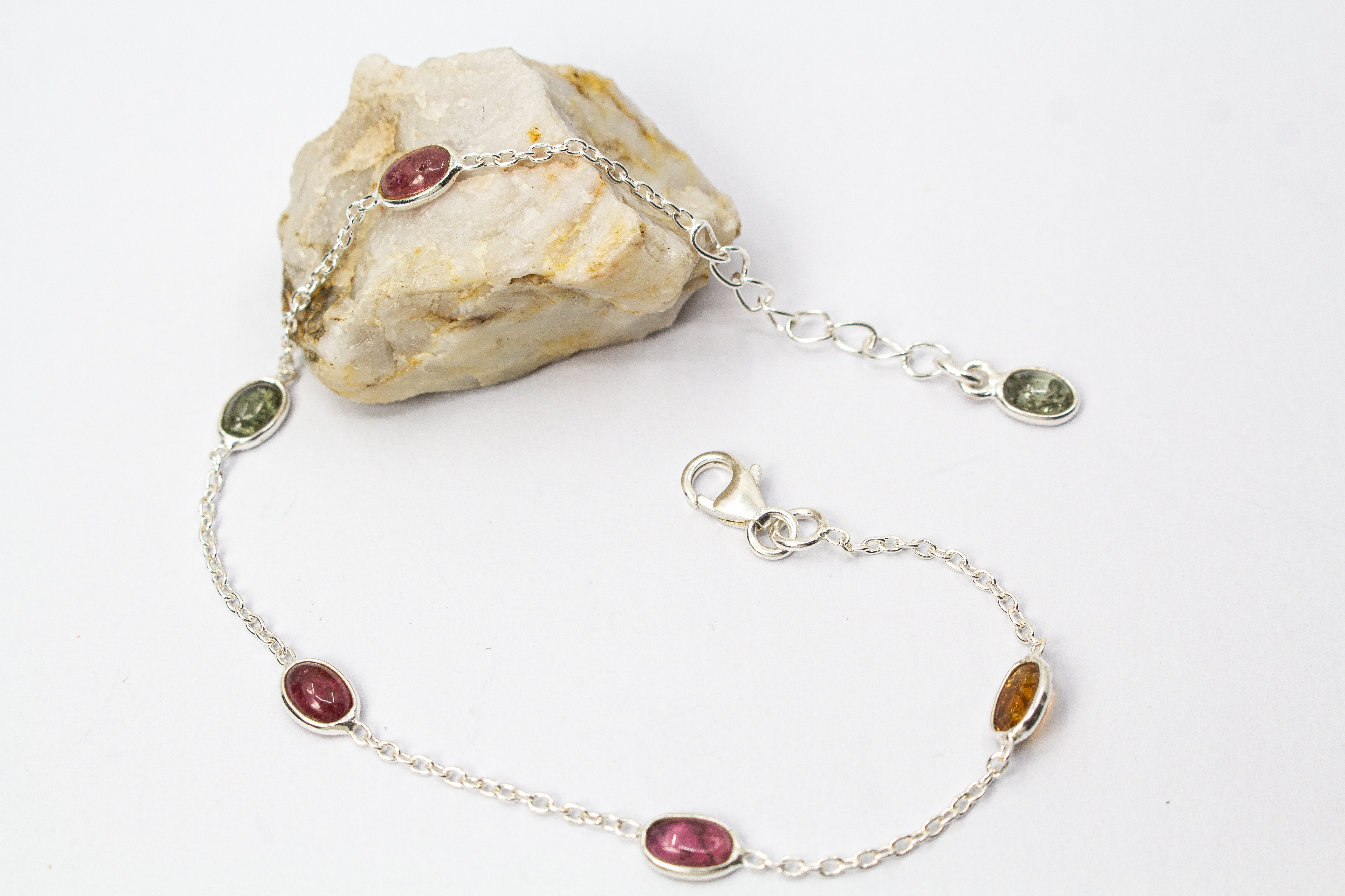 Das filigrane Silber-Armband „Indian Summer“ aus der Goldschmiede Regina Kraus, flach auf weißem Untergrund arrangiert. Die feine Kette aus rhodiniertem 925er Sterlingsilber verbindet fünf ovale Turmalin-Cabochons in den warmen Farben Weinrot, Moosgrün, R