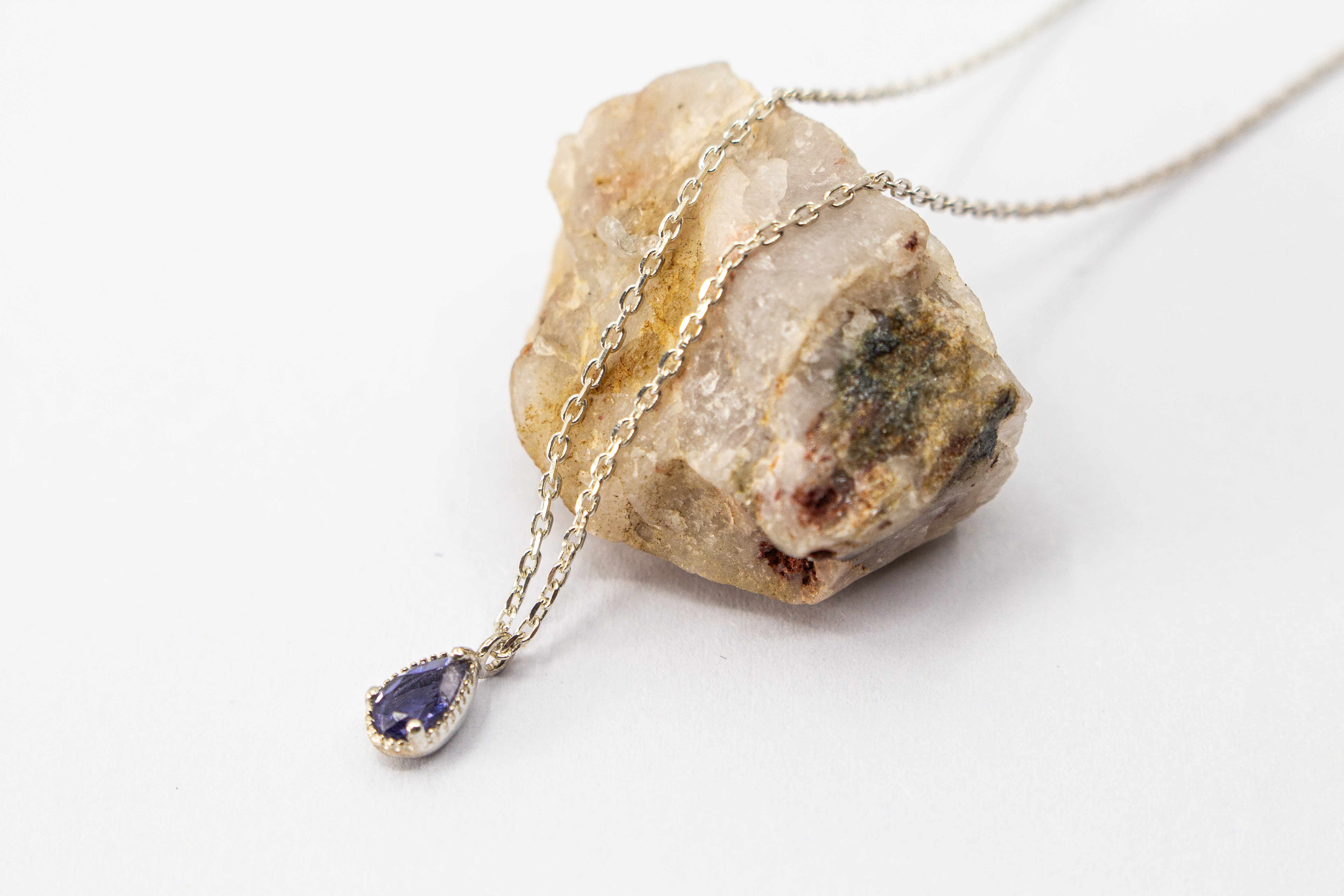 Filigrane Halskette aus 925 Sterling Silber mit einem kleinen, tropfenförmigen, facettierten blau-violetten Iolith-Edelstein in einer fein verzierten Fassung aus dem Online-Shop der Goldschmiede Regina Kraus.